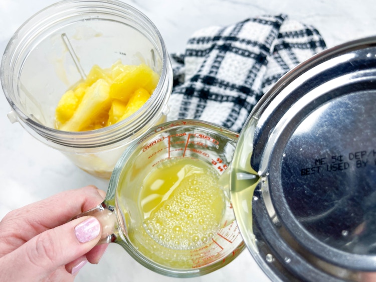 a person pouring canned pineapple juice into a measuring cup 