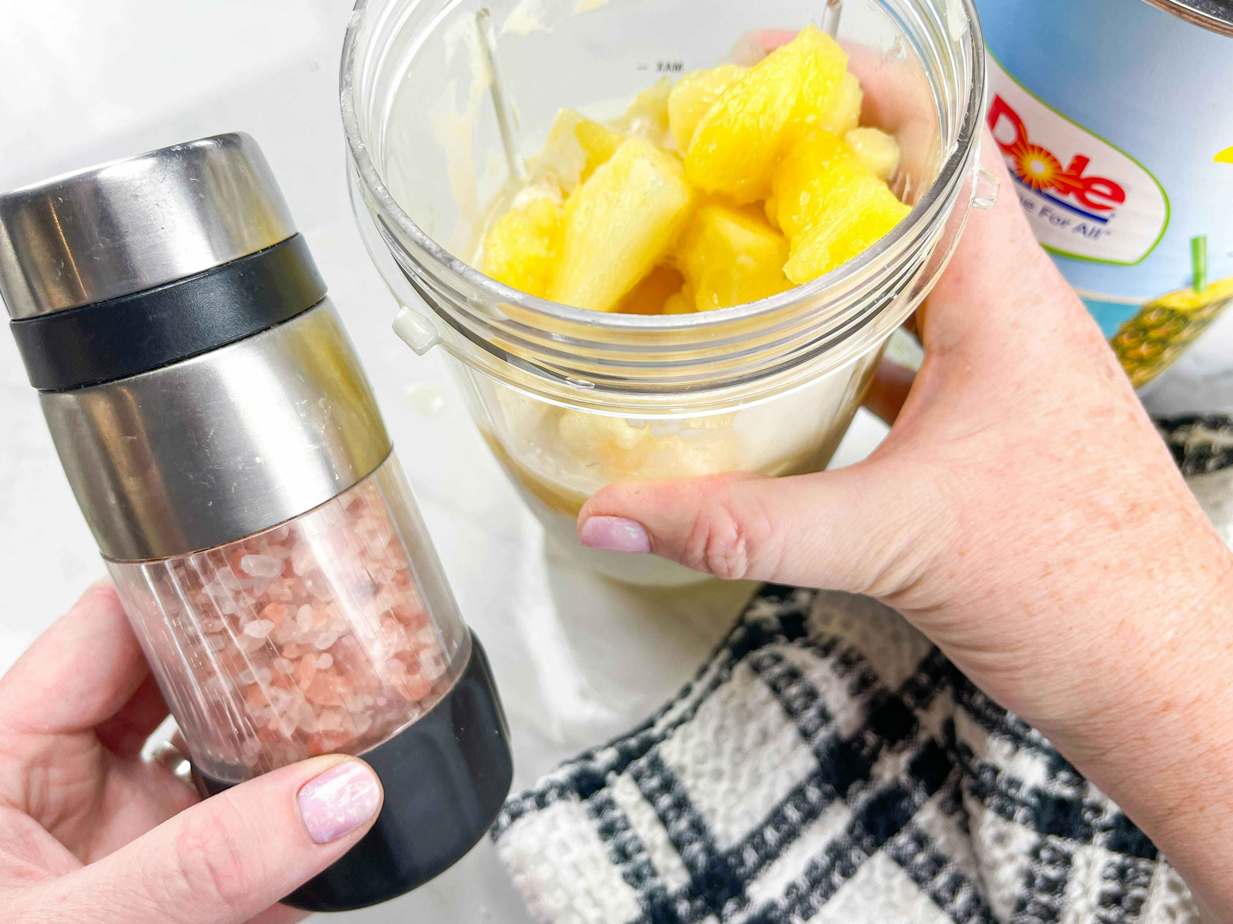 a person holding salt next to a blender cup with frozen pineapple inside 