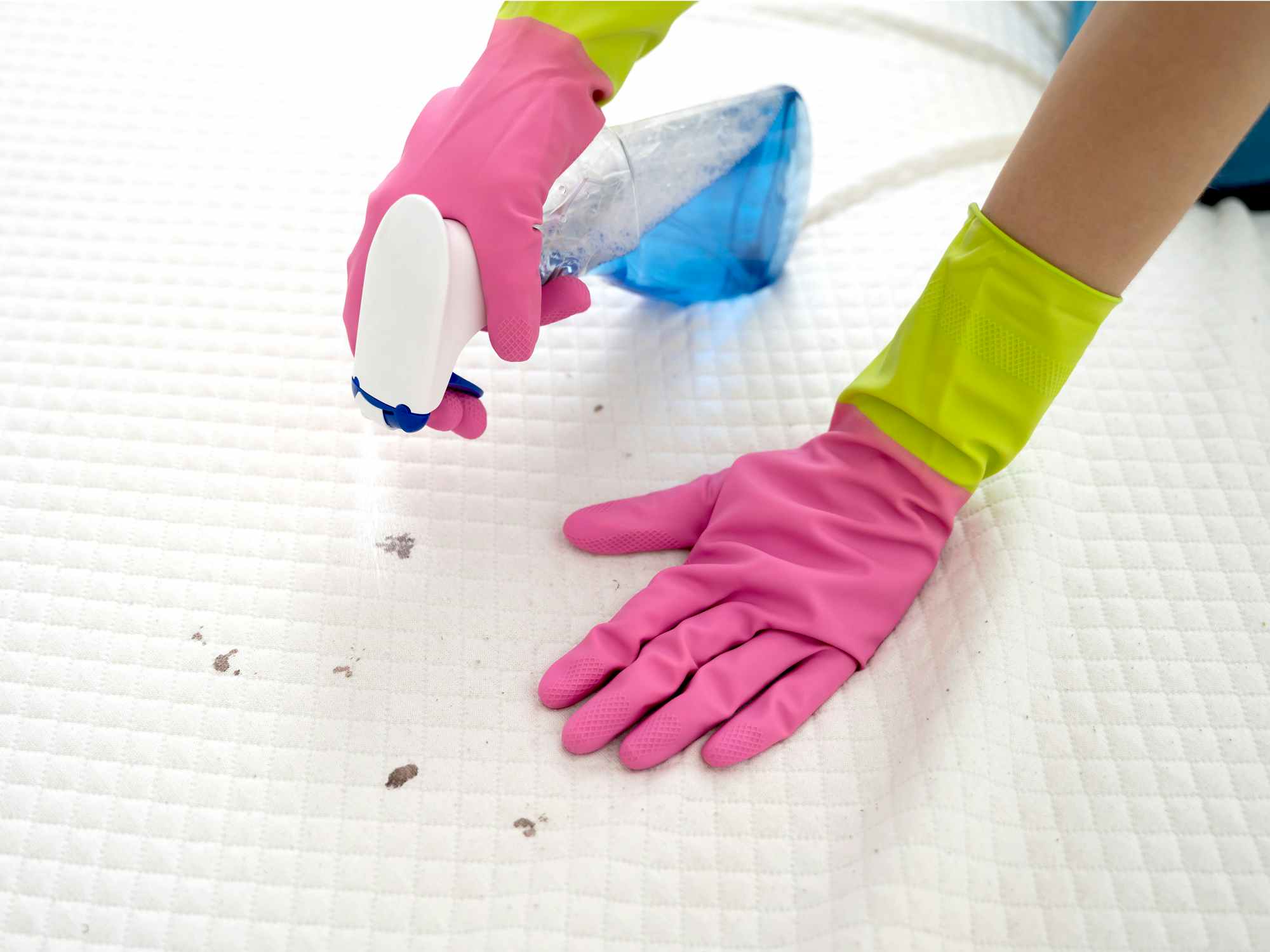 person with gloves spraying cleaning solution on mattress