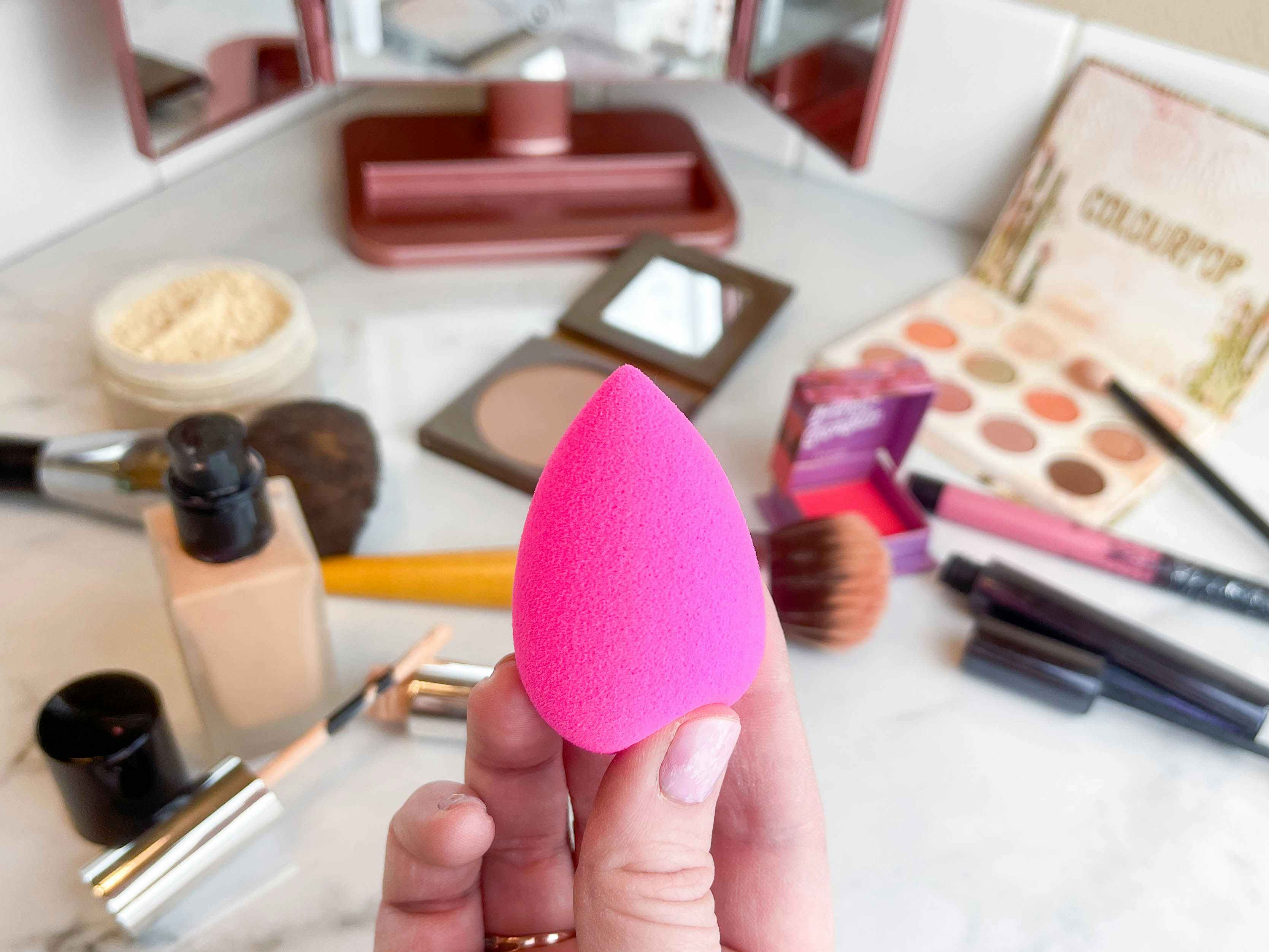 a person holding a beauty blender in front of makeup on a counter 