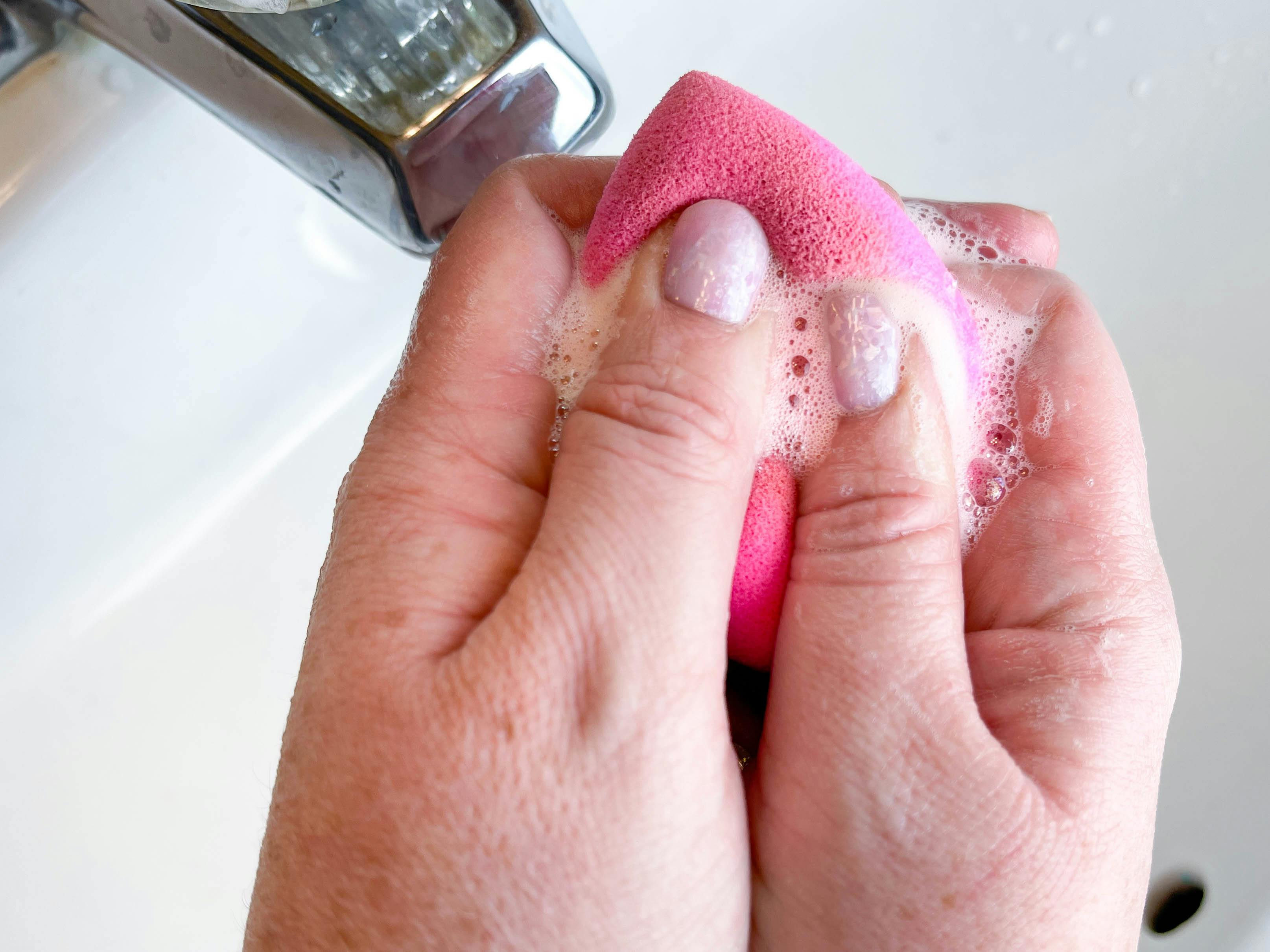 a person squeezing a beauty blender under running water 