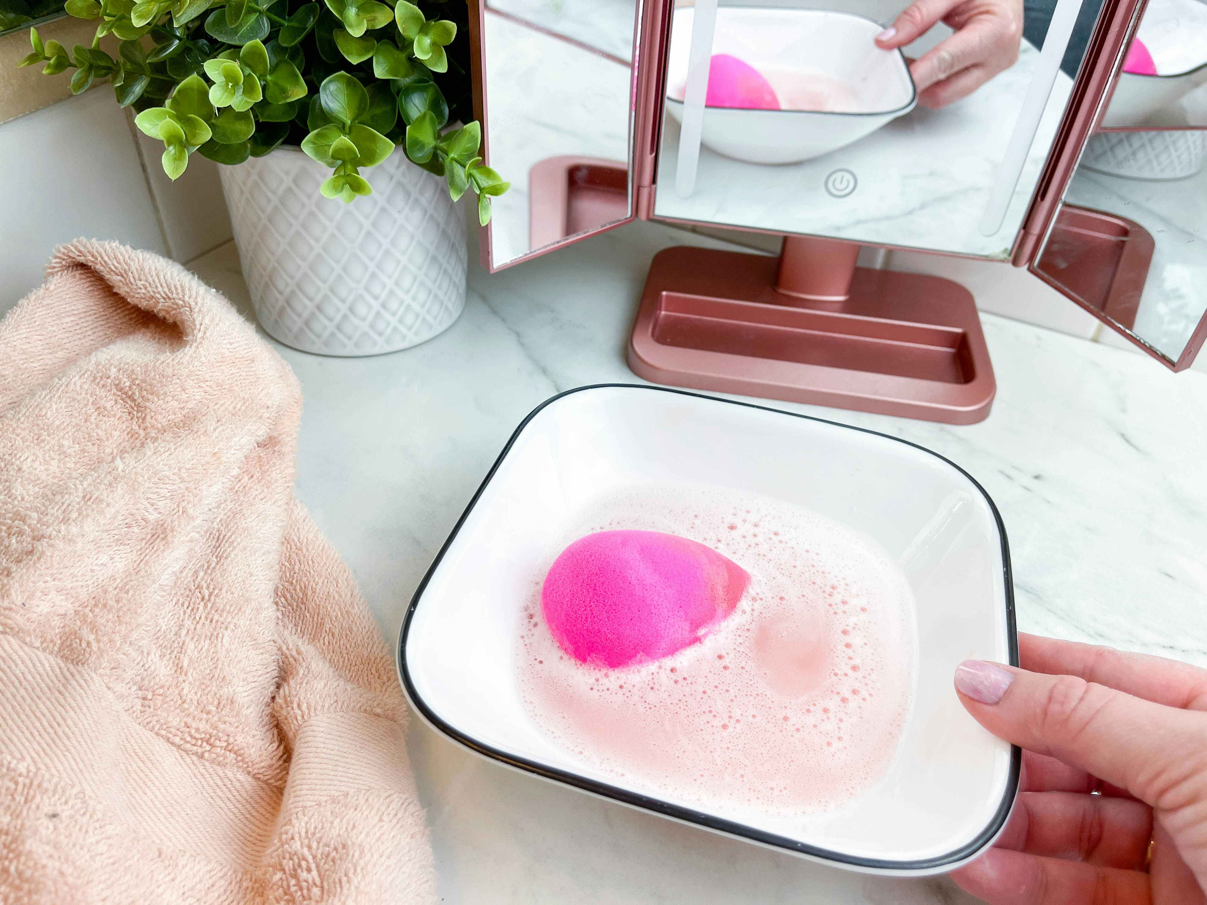 a person placing a beauty blender into a bowl of water 