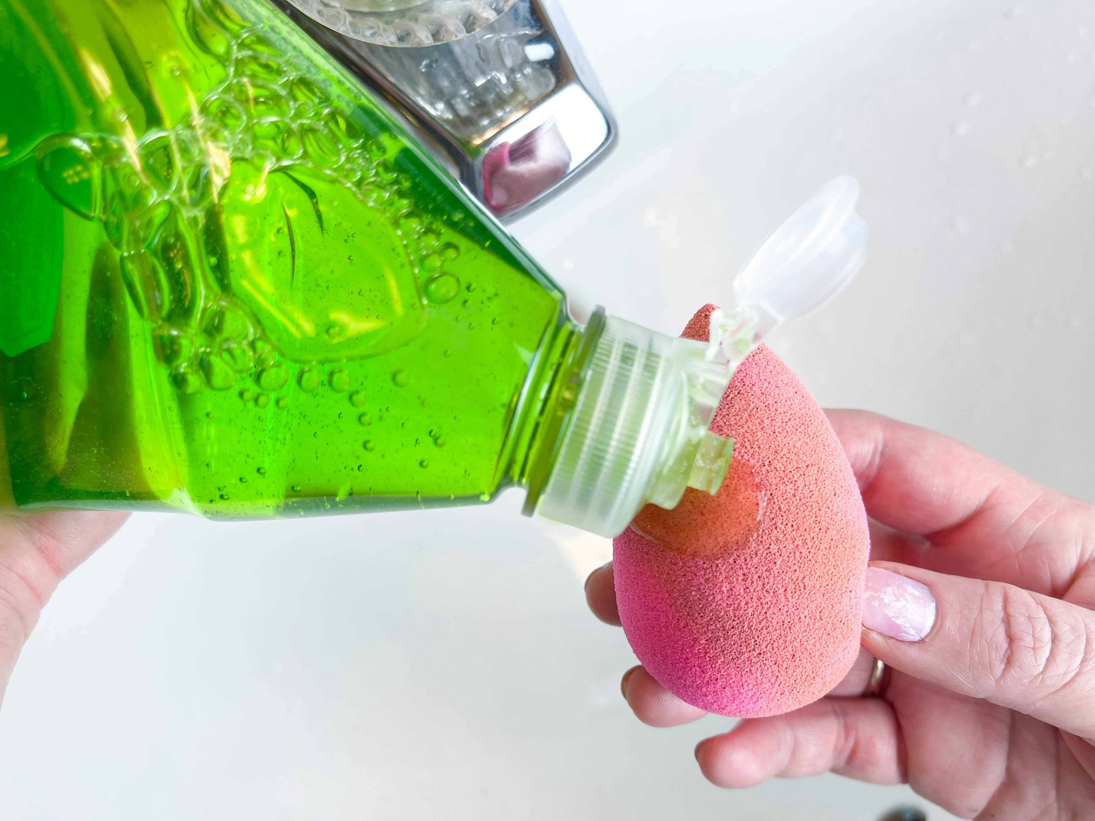 a person putting dish soap onto a dirty beauty blender 