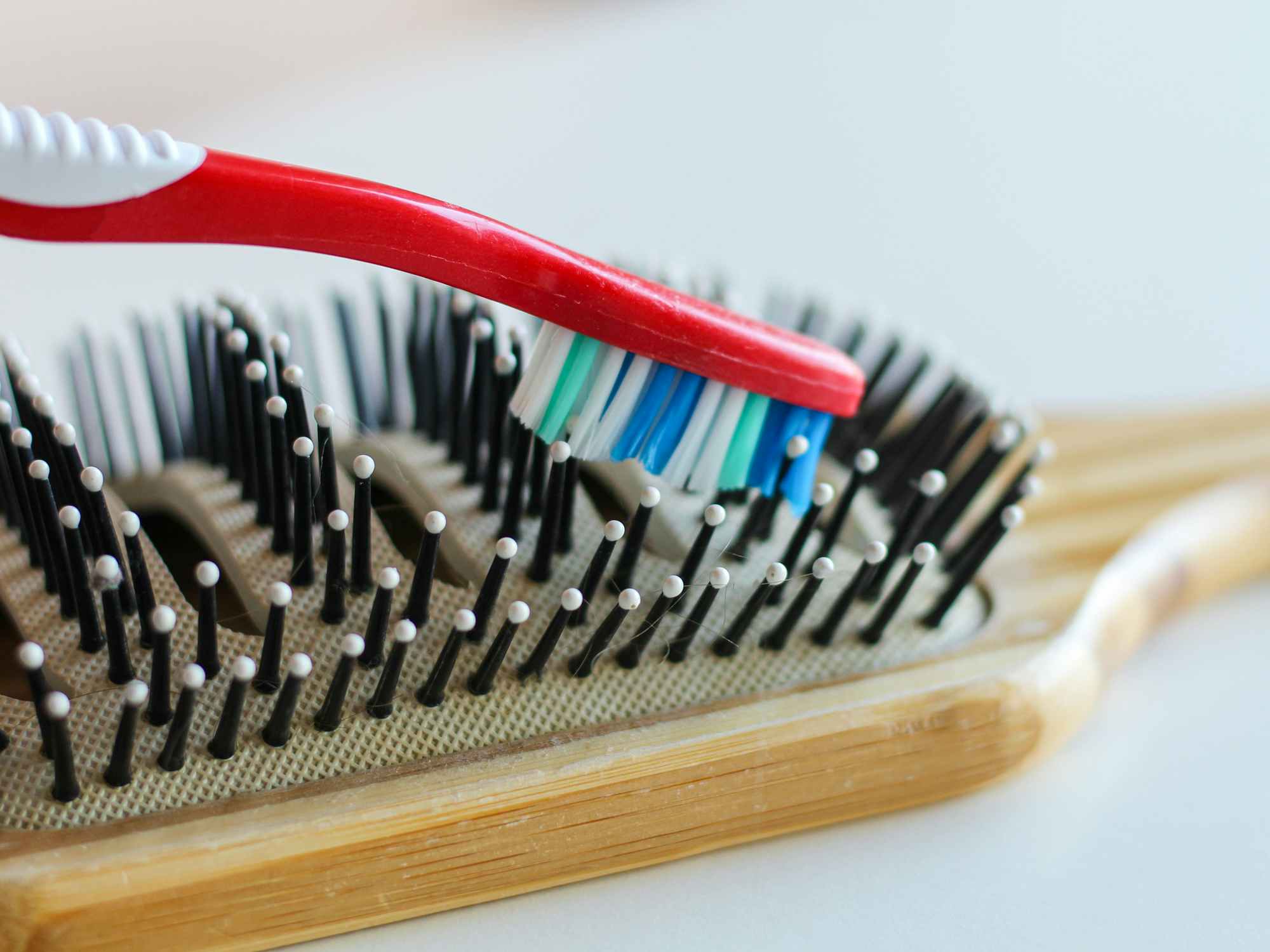 a toothbrush cleaning the bristles of a wooden hairbrush
