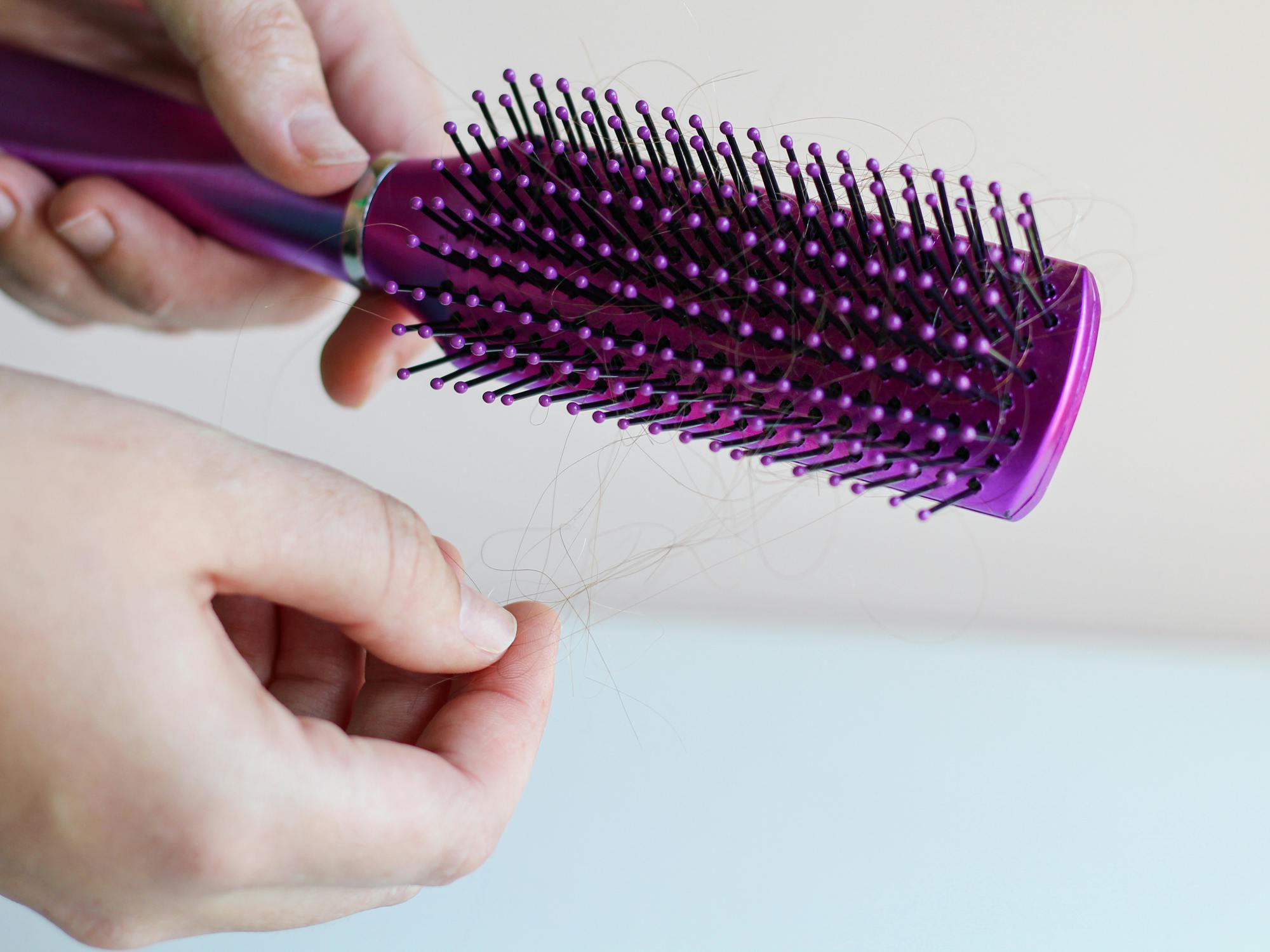 person removing hair from a hairbrush to clean it