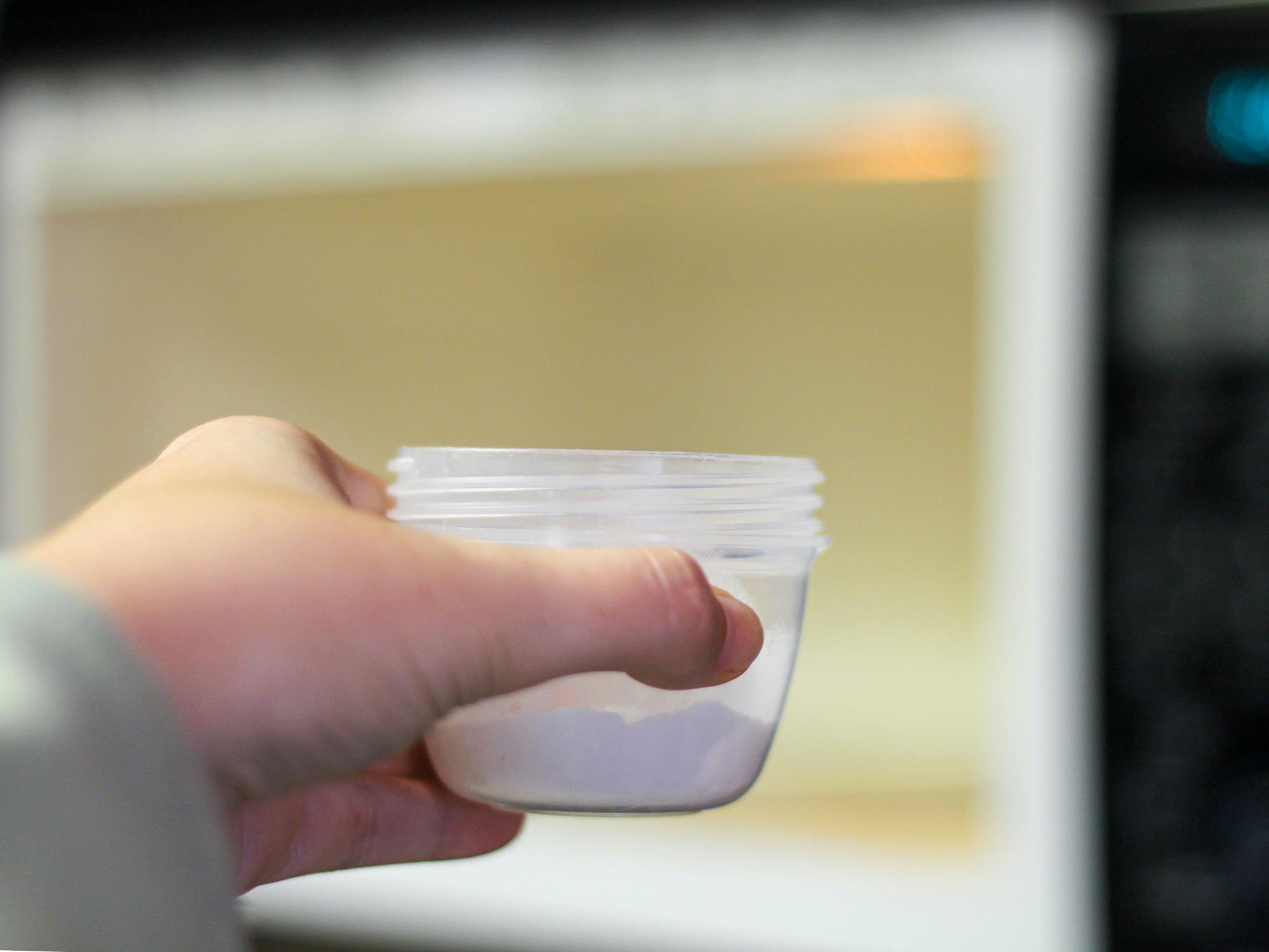 a person putting a small bowl of baking soda into a microwave to absorb the smell