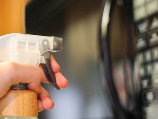 a person spraying the exterior of a microwave with a vinegar mixture