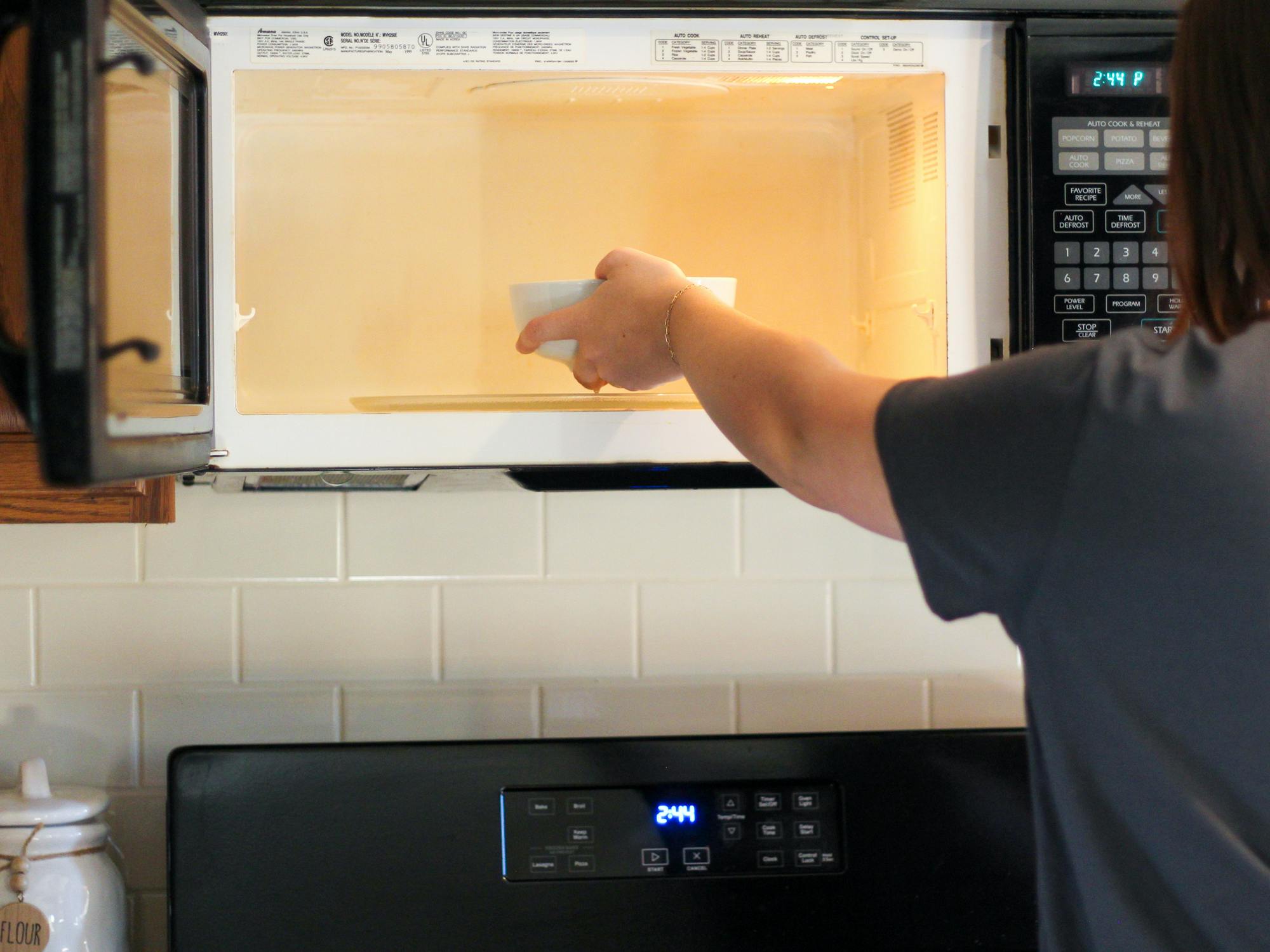 a person placing a bowl of vinegar into a microwave to clean it