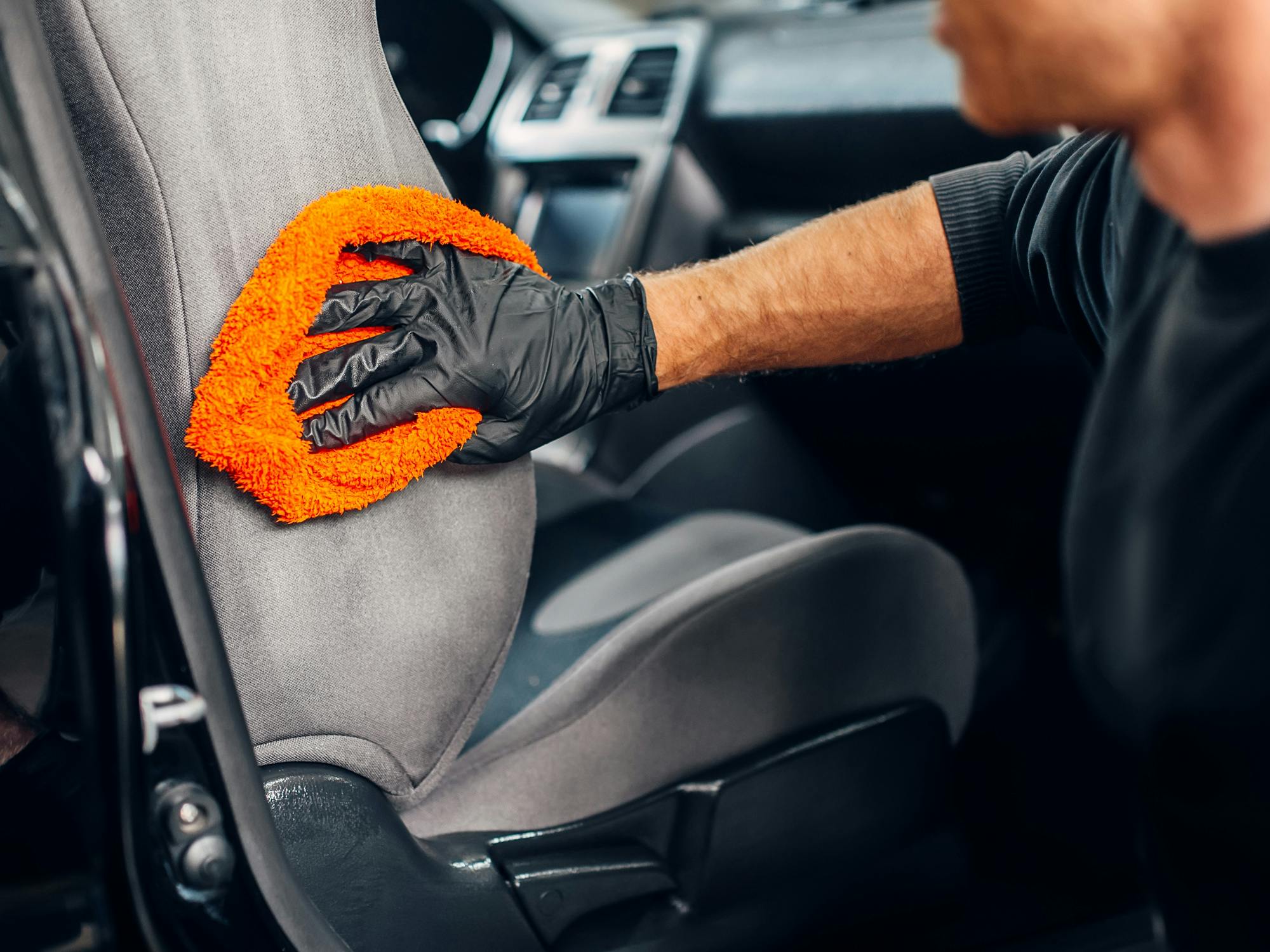 person cleaning a car seat with an orange towel