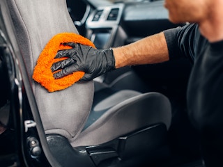 person cleaning a car seat with an orange towel