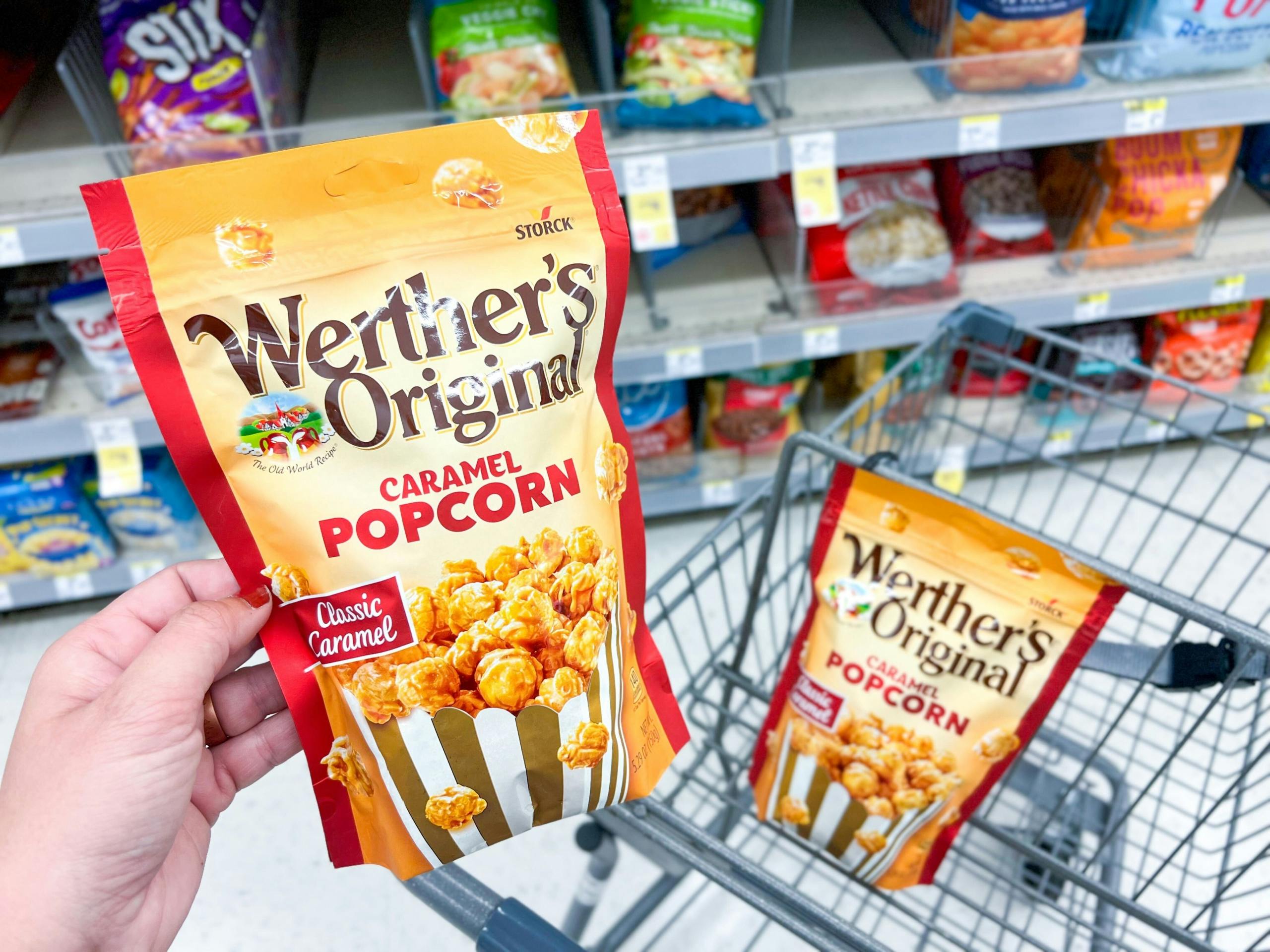 hand holding bag of werthers popcorn with another bag of popcorn in shopping cart