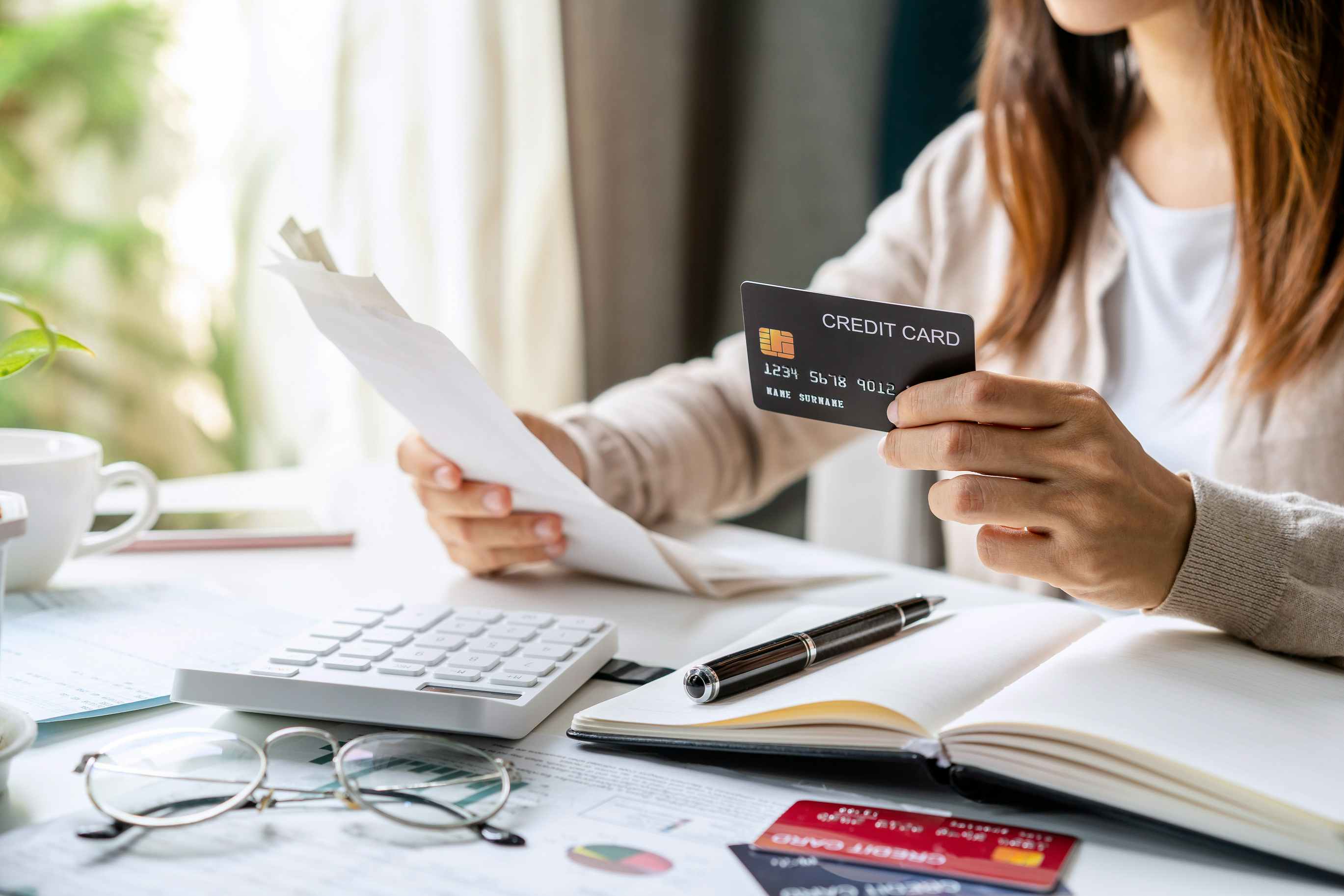 A person holding a credit card and looking at a bill with a calculator and documents on the table