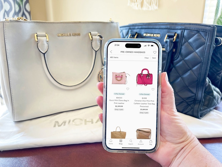 Someone looking at the Preowned Handbags on the Saks Off 5th app in front of some designer handbags on a table