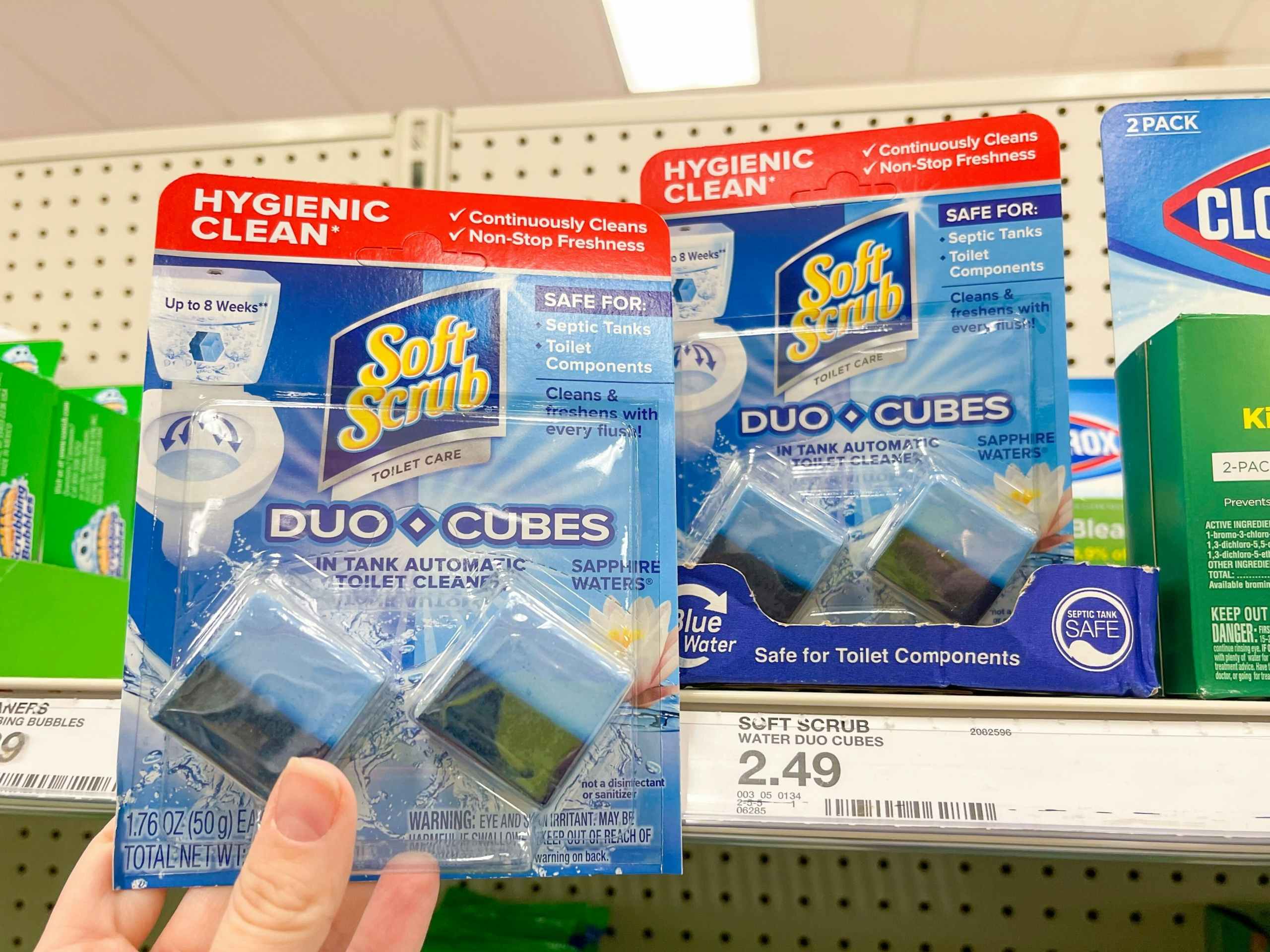 A package of Soft Scrub Duo Cubes held out by hand in front of other Soft Scrub Duo Cubes sitting on a store cart.