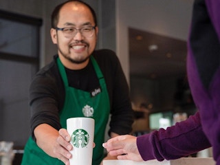 Starbucks barista handing a cup to a customer while smiling