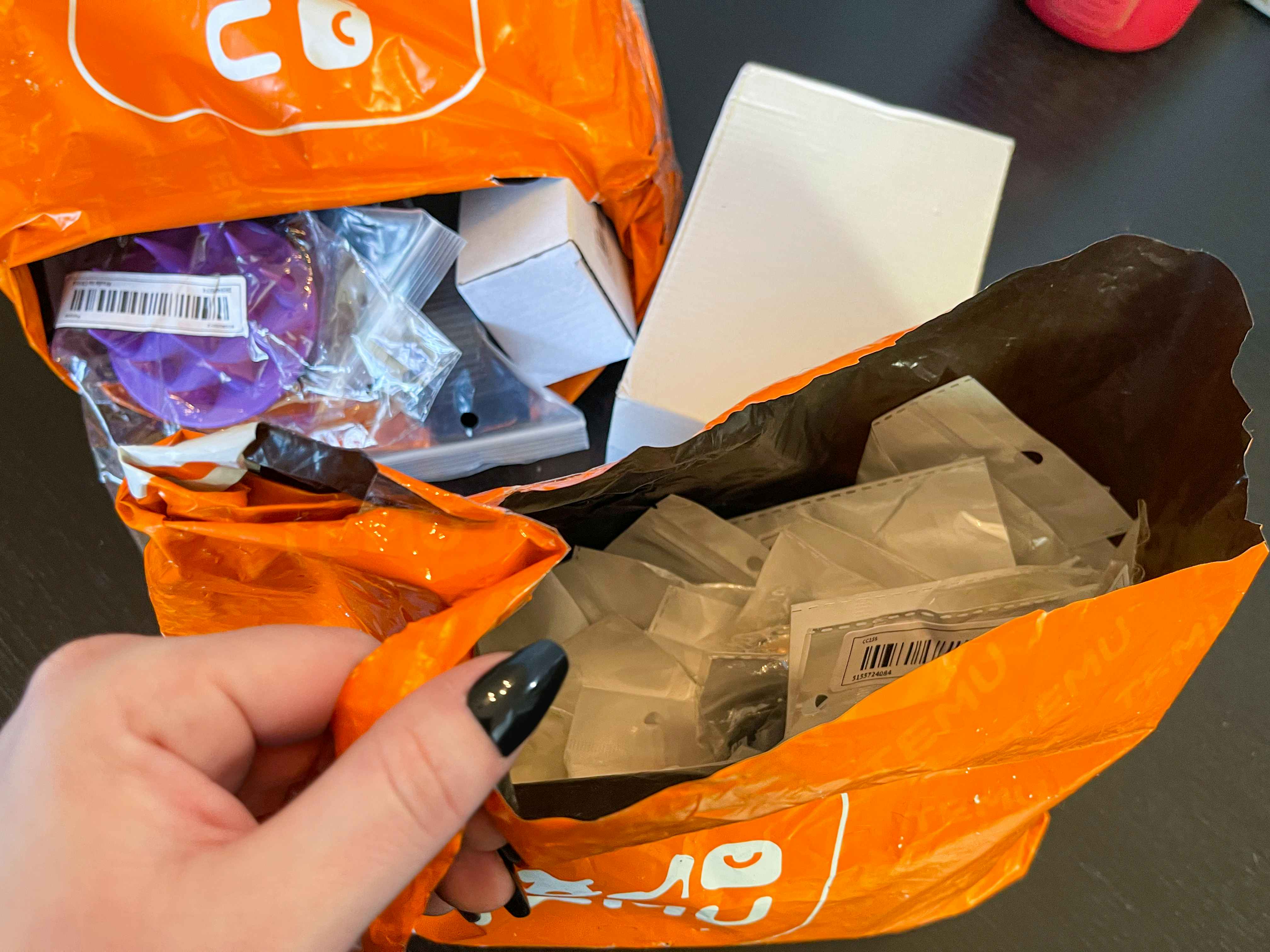 A womans hand holding up an orange Temu shipping package filled with Temu items