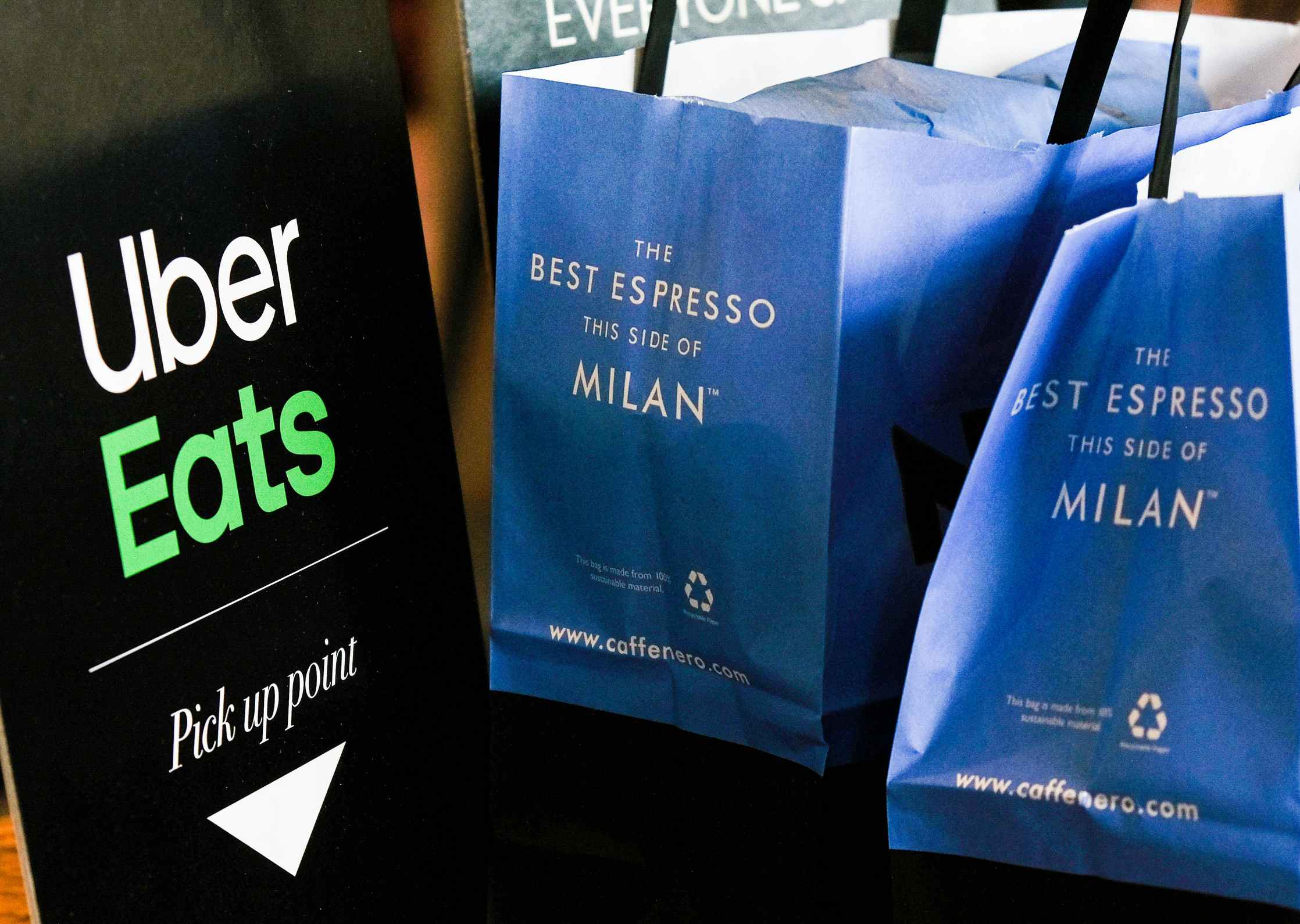 An Uber Eats sign next to two bags from Caffe Nero in Milan next to it