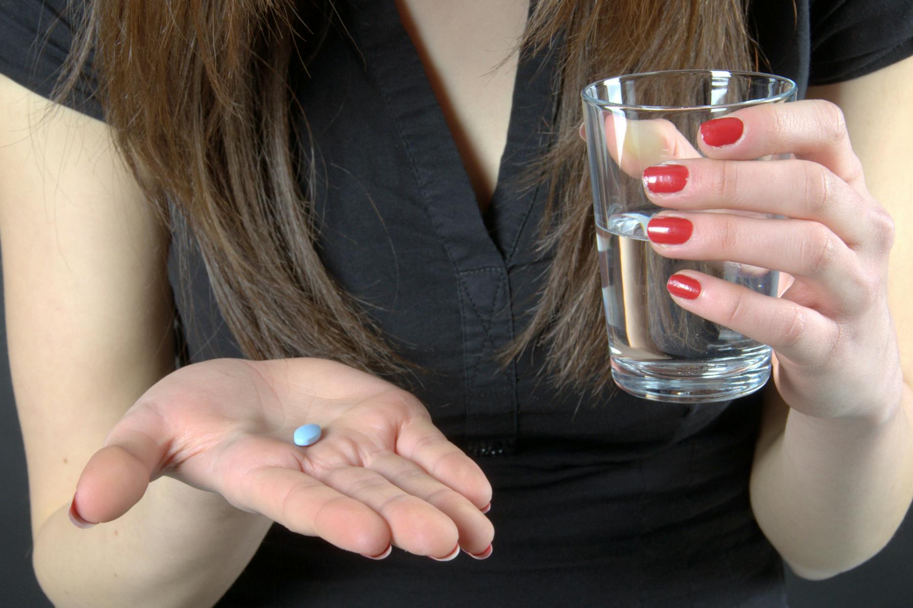 Someone holding a glass of water about to take a blue tablet medication