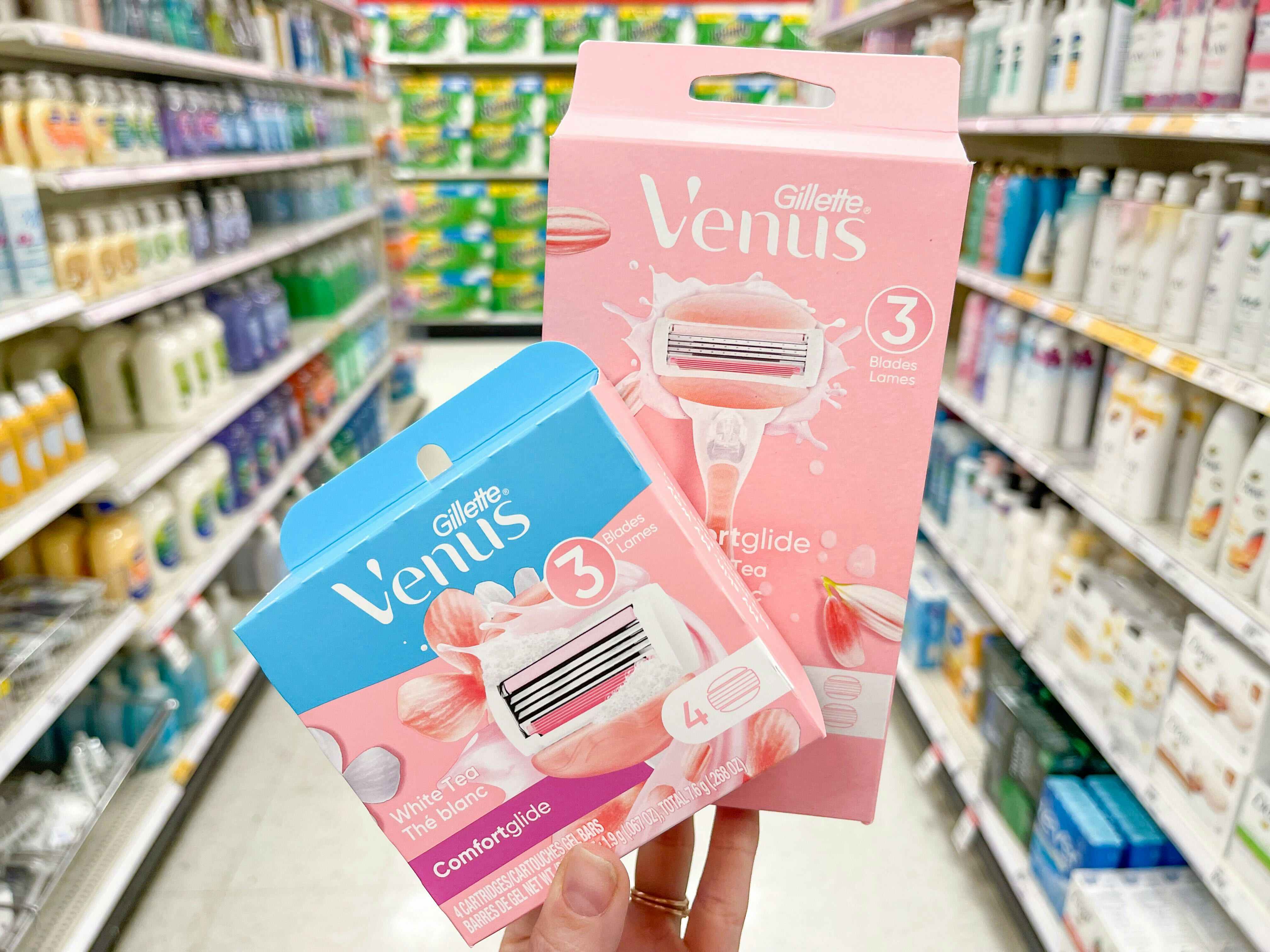 A Venus White Tea razor and a Venus refill pack held out by hand in front of a store aisle.