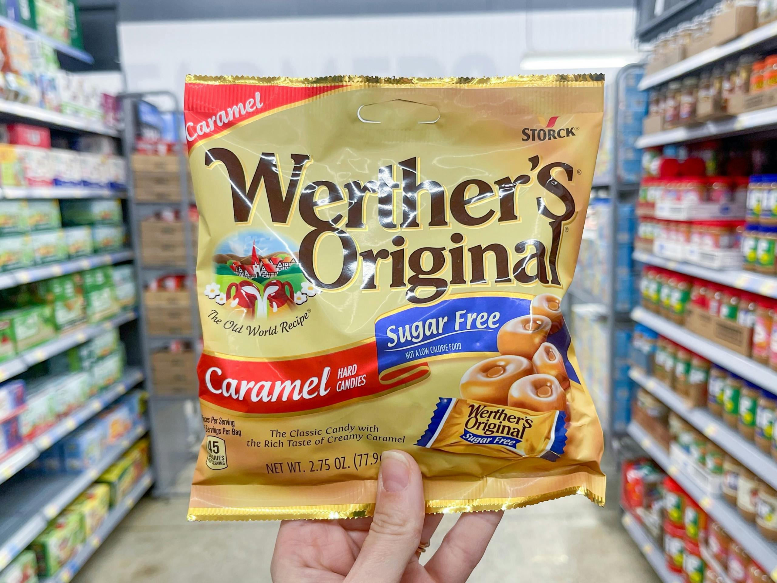A Werther's Original candy package held out by hand in front of a store aisle.
