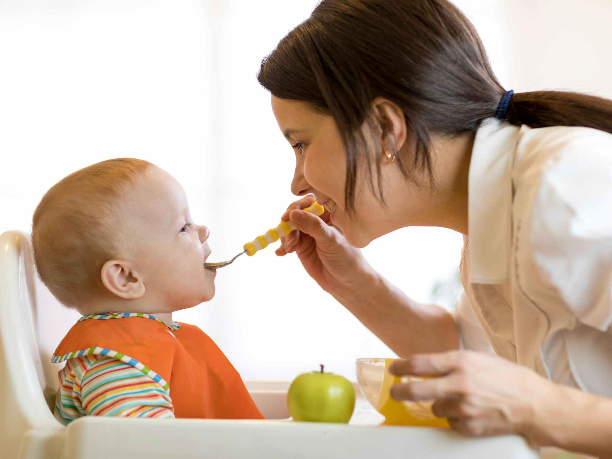 Mom giving fruit puree to her baby in a high chair