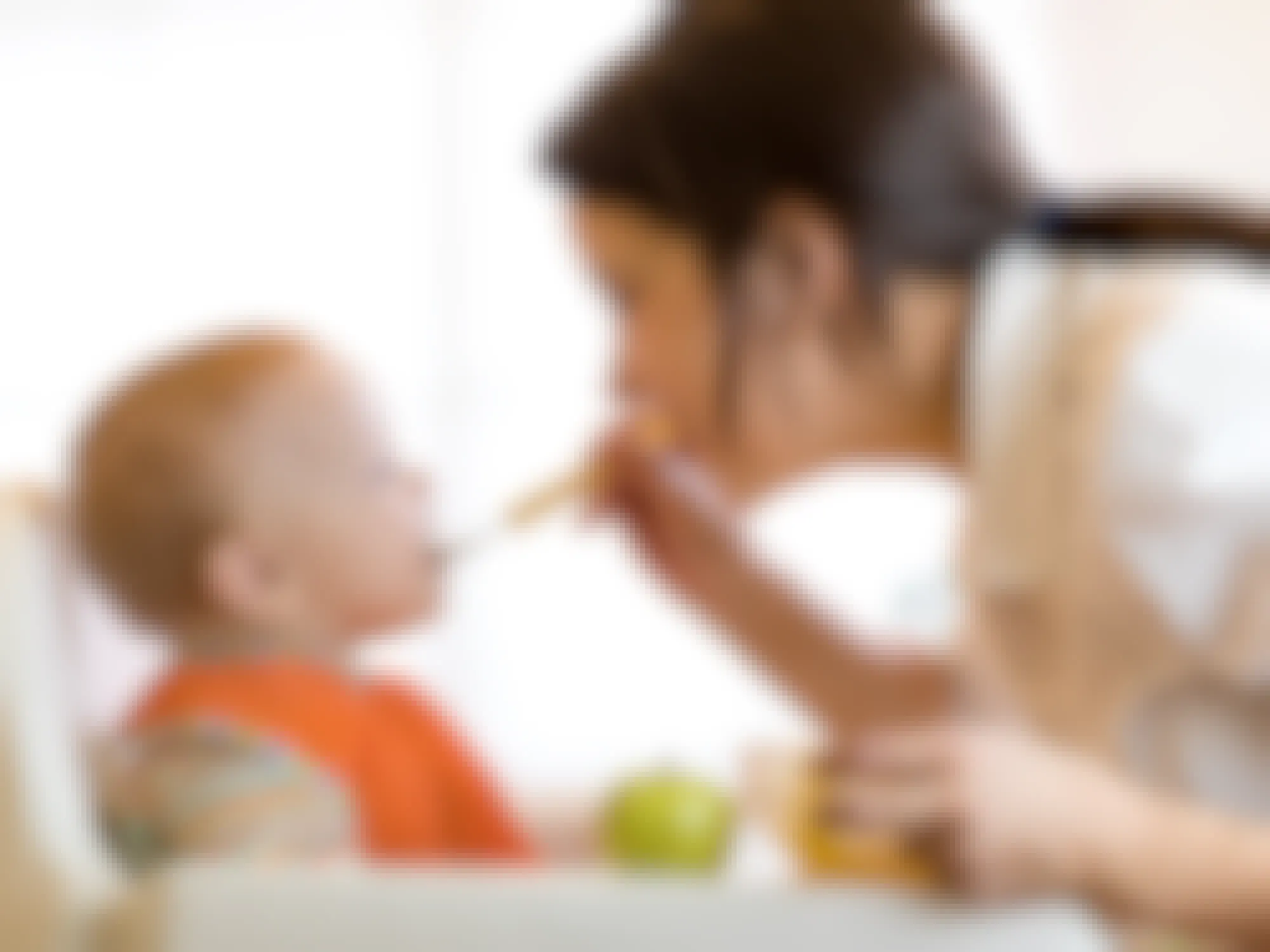 Mom giving fruit puree to her baby in a high chair