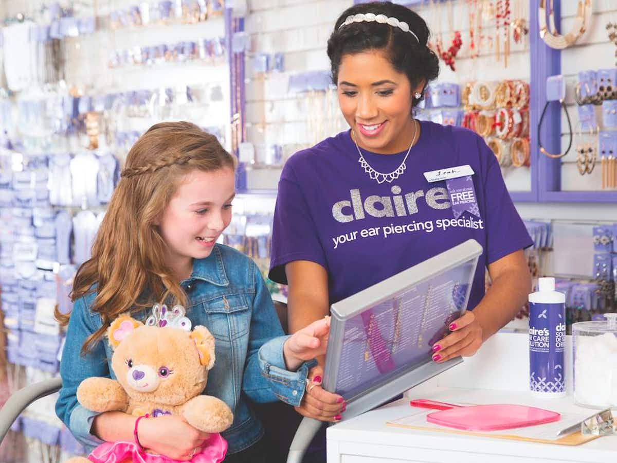 A Claire's employee helping a child pick out earrings for her piercings