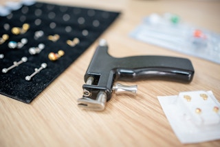 A piercing gun on a counter with some earrings and other body jewelry