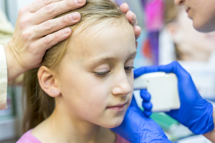 A young girl getting her ears pierced with a piercing gun