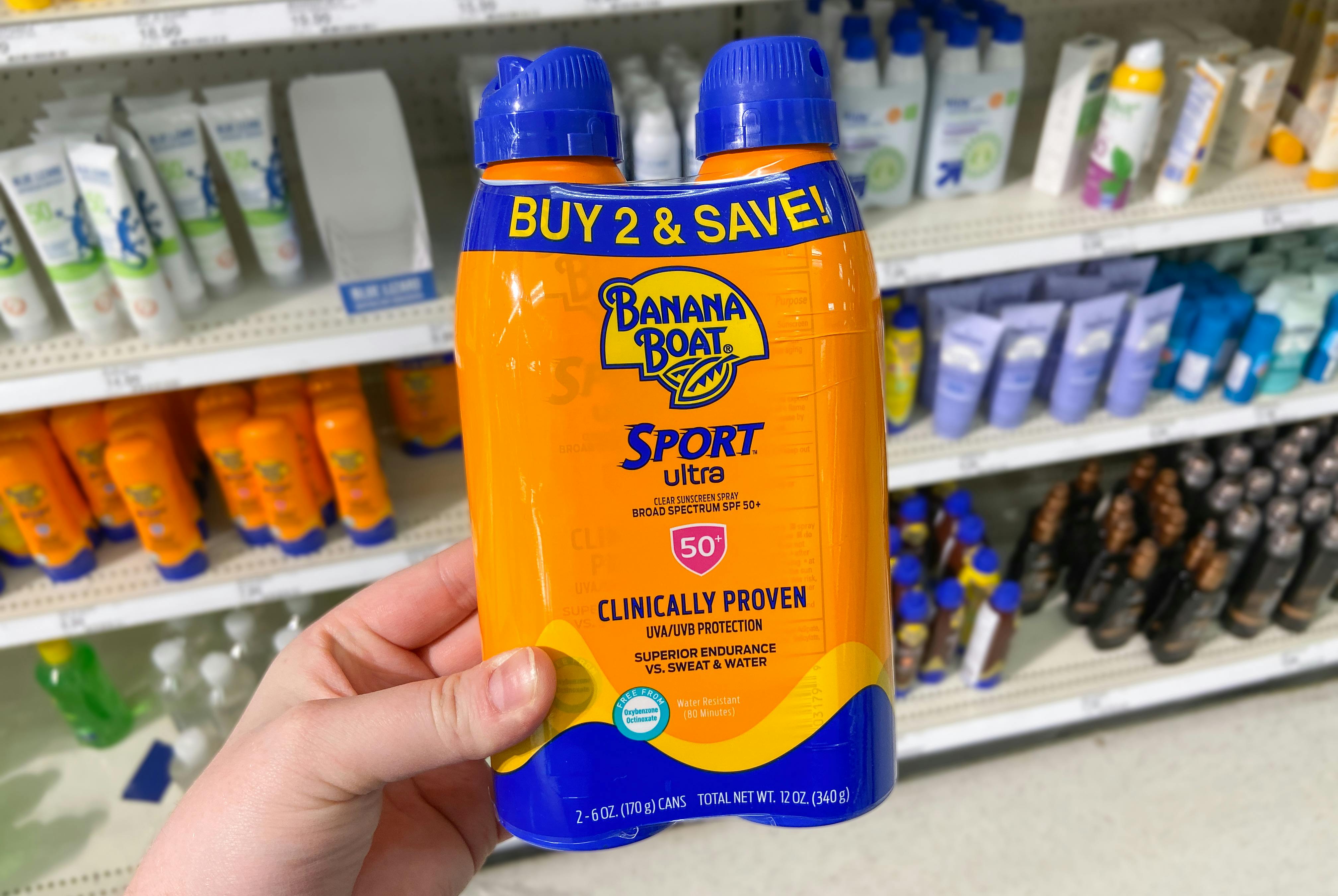 hand holding a two pack of banana boat sunscreen spray in front of a sunscreen display