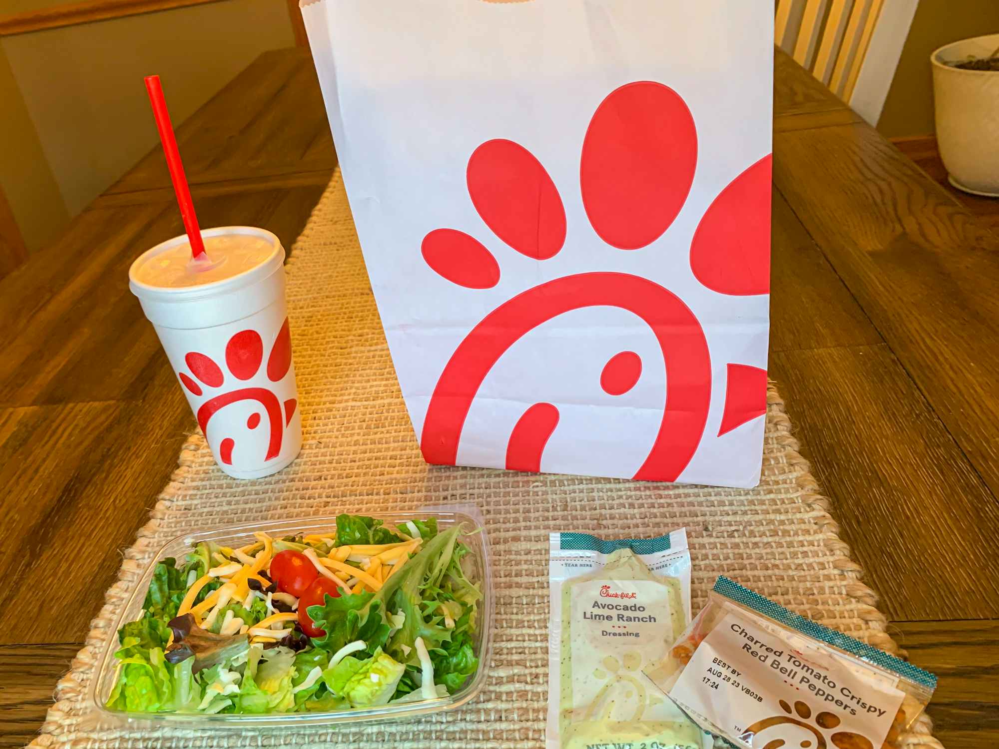 a chick fil a side salad sitting next to a chick fil a bag and drink