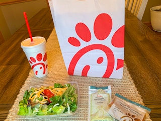 a chick fil a side salad sitting next to a chick fil a bag and drink