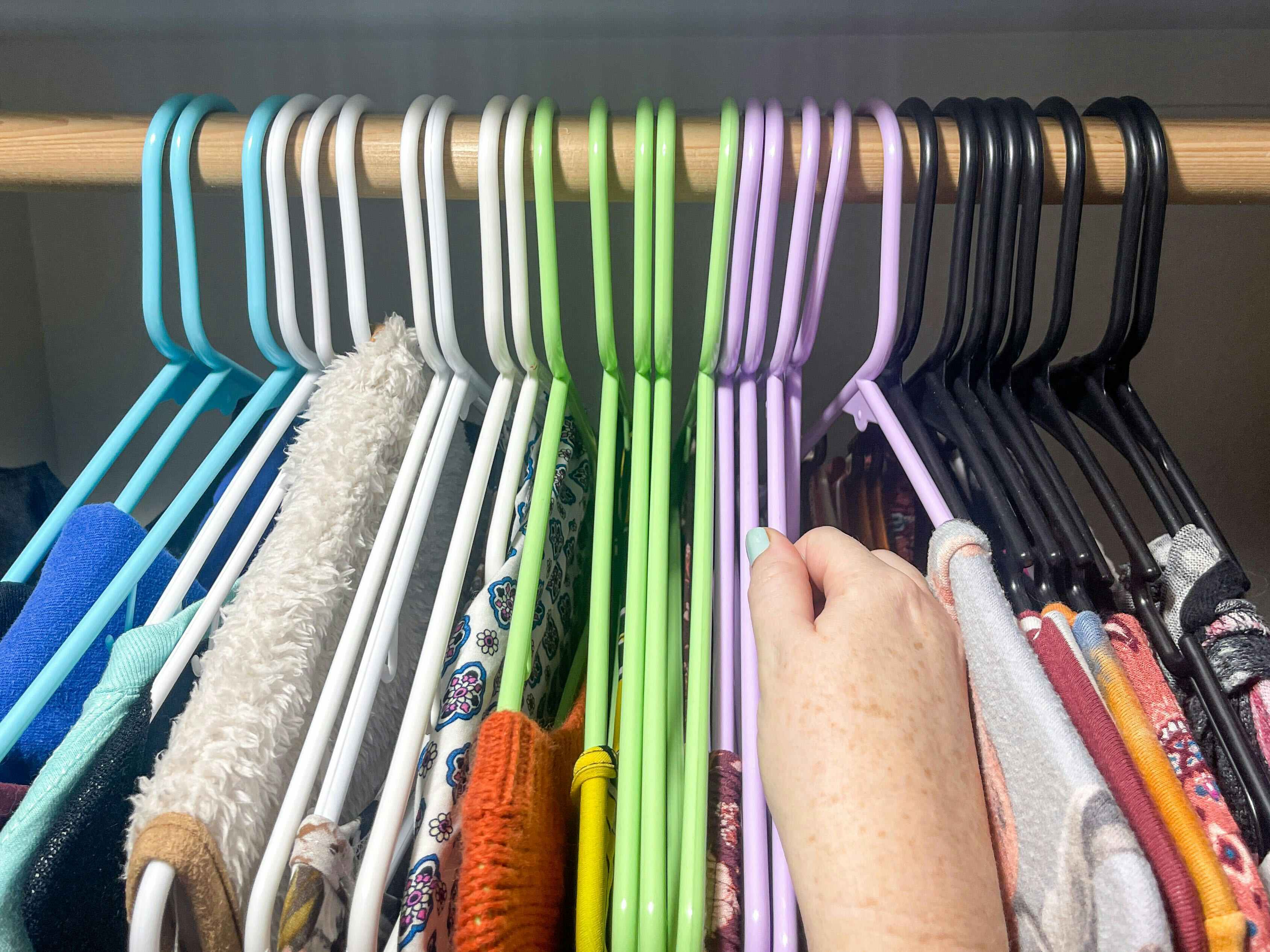 a person's hand grabbing a colored hanger in a closet