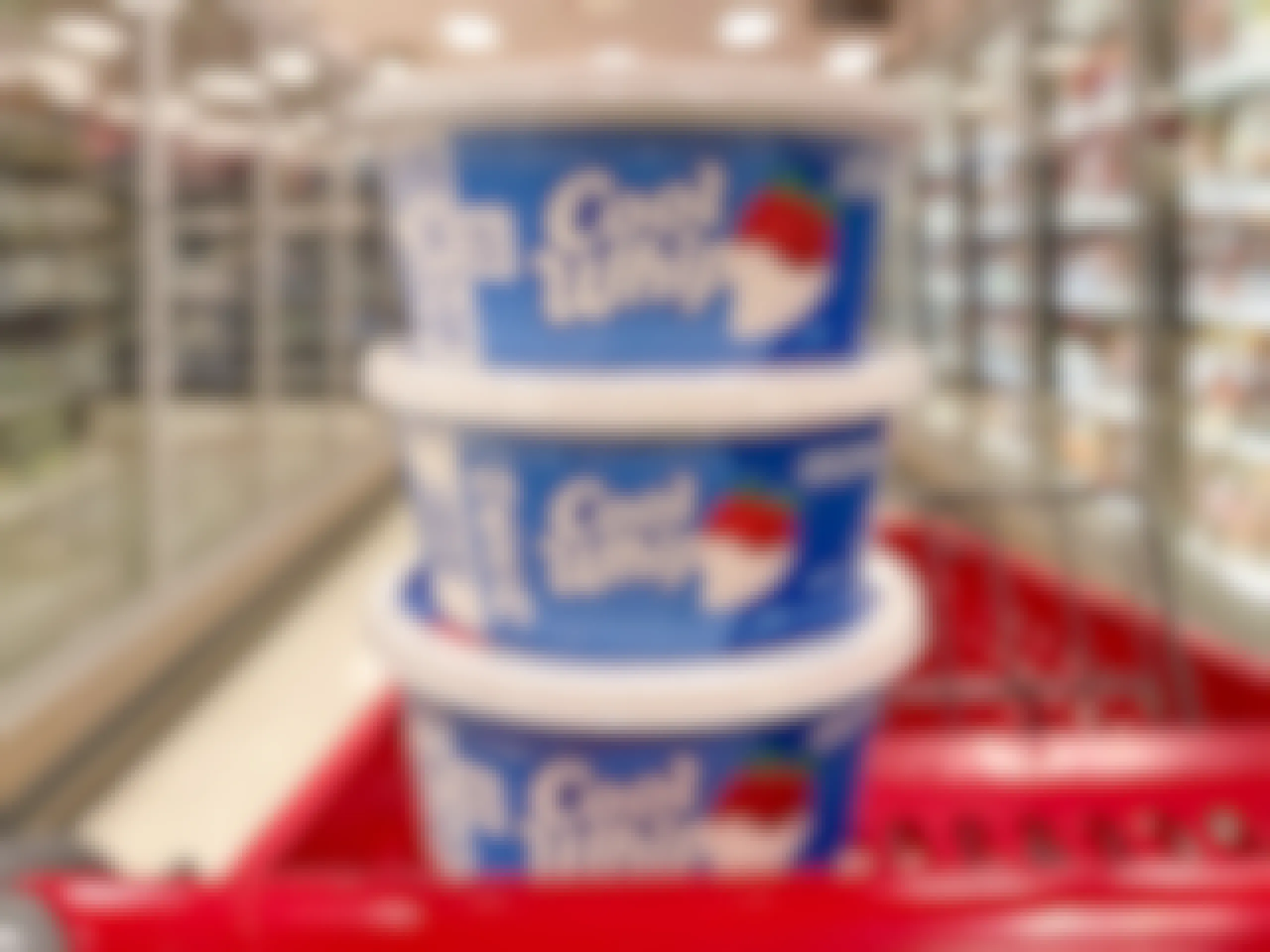 Three containers of Cool Whip stacked on top of each other sitting on a store cart in the middle of a shopping aisle