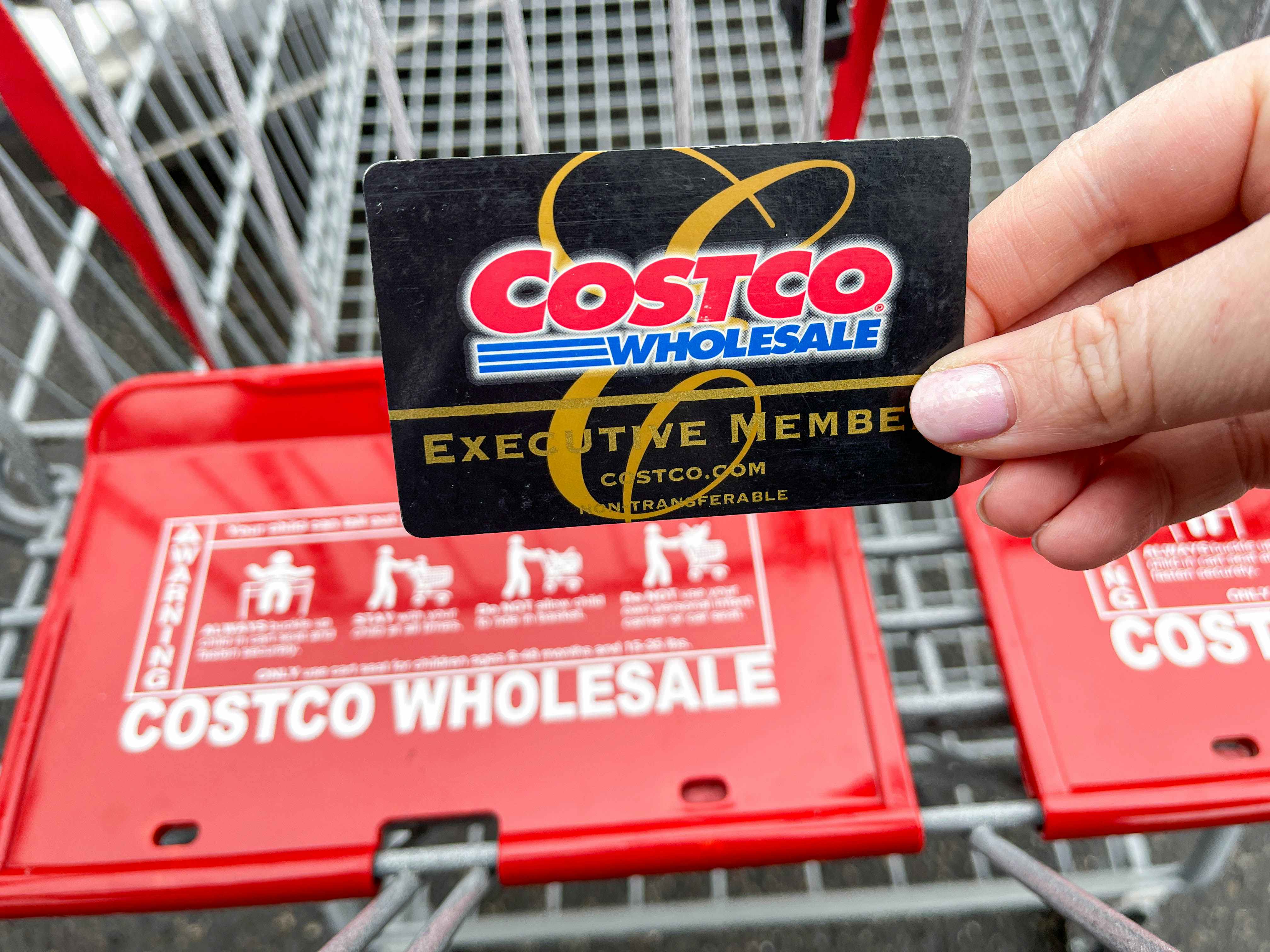 a person holding up a costco shopping card in front of a shopping cart