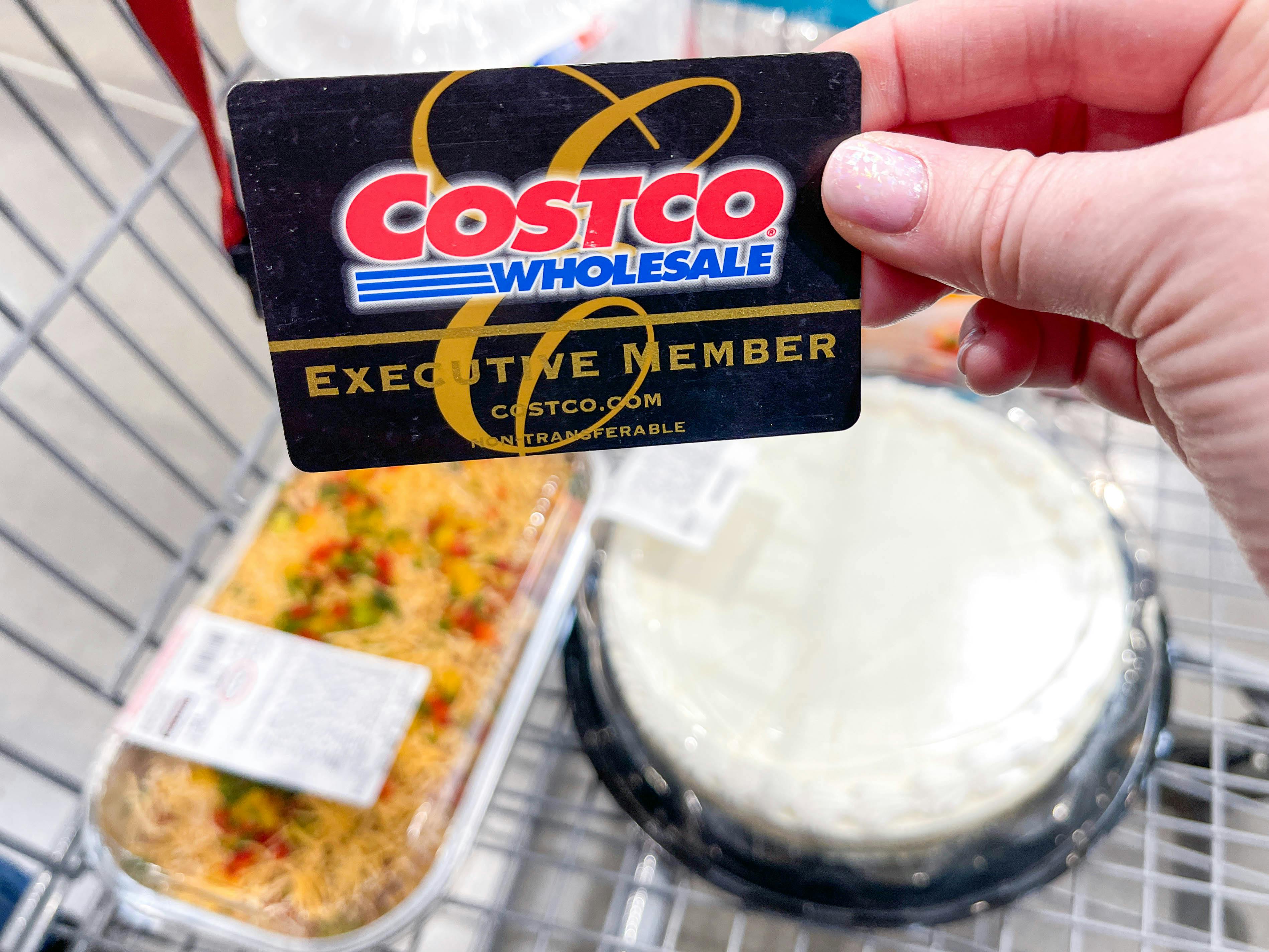 A person holding a costco membership card in front of a cart with meals inside 