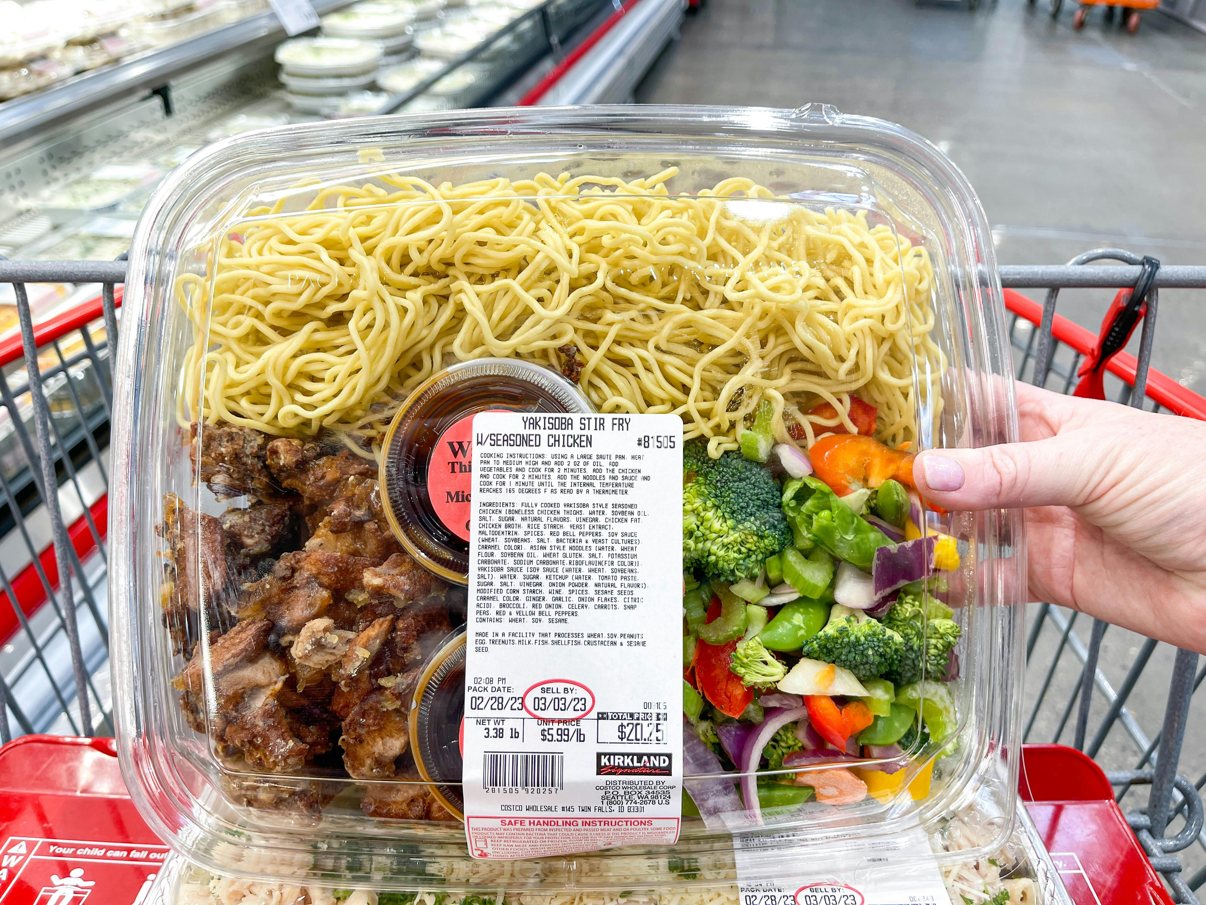 a person holding up a costco prepared meal in cart 