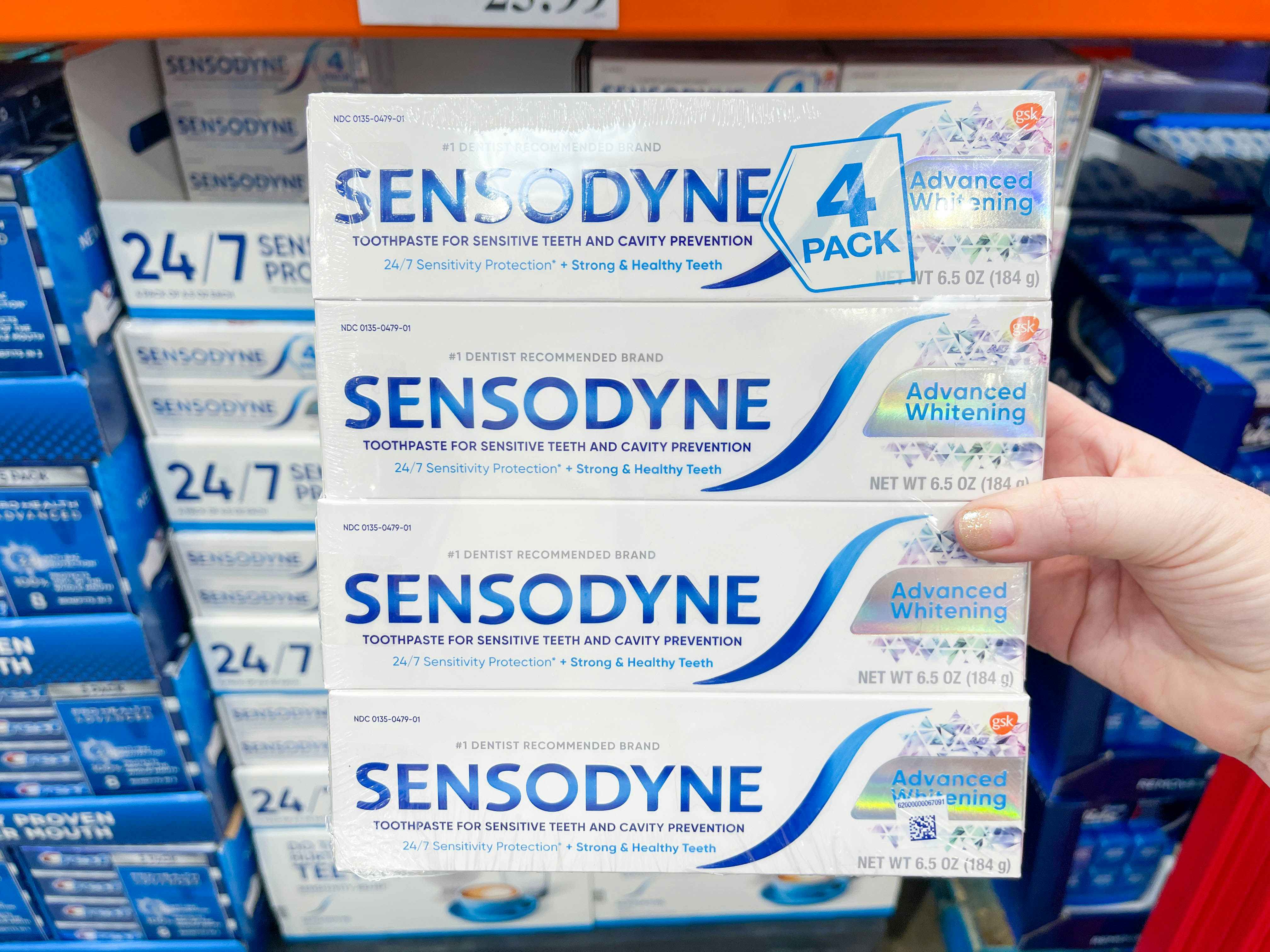 four boxes of toothpaste packaged together being held in store