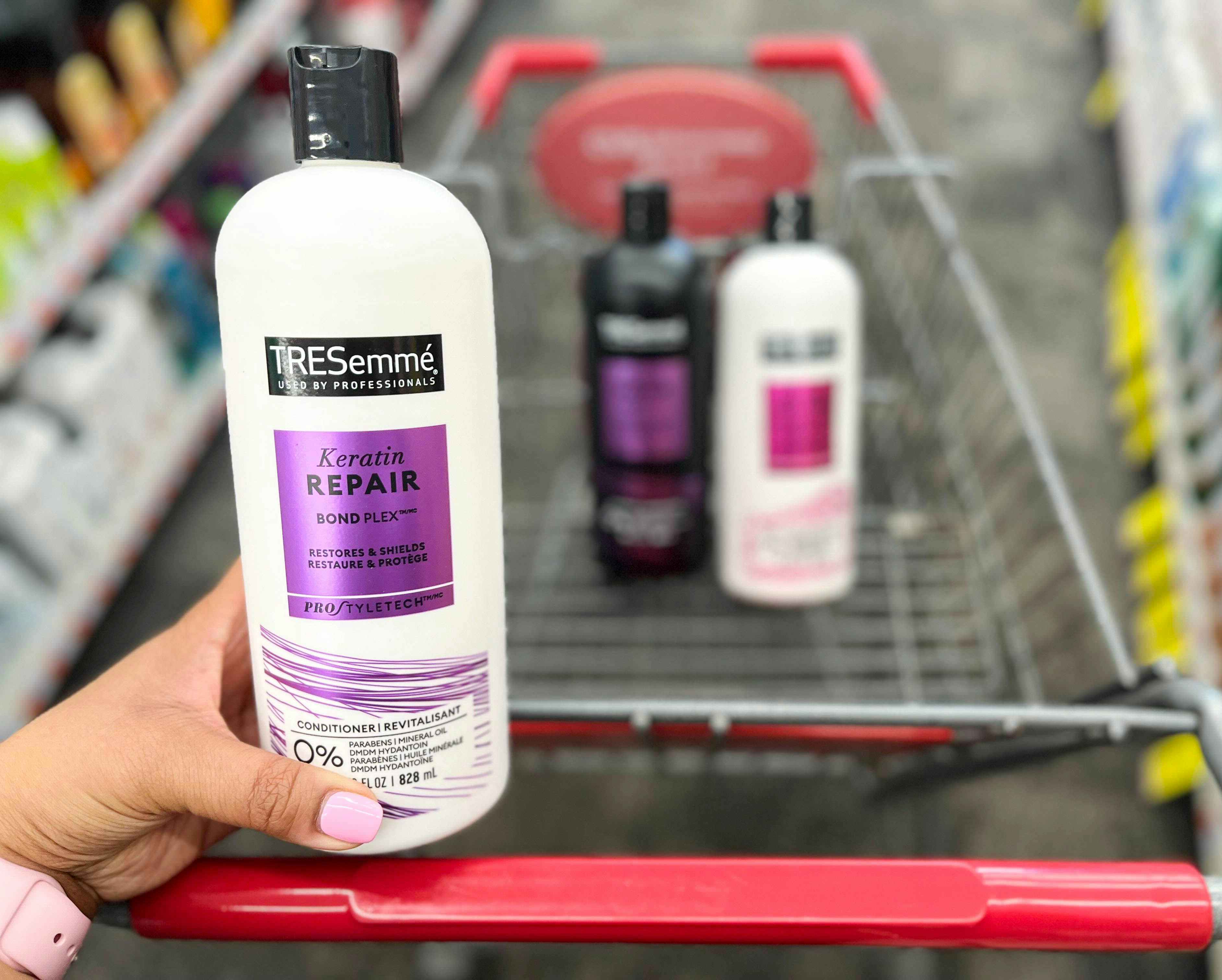 hand holding bottle of Tresemme conditioner in front of shopping cart with Tresemme shampoo and conditioner inside