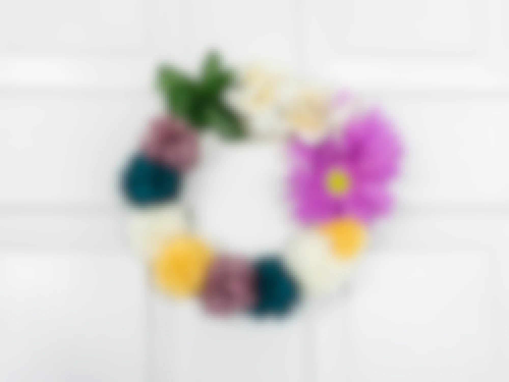 A completed DIY Pompom floral wreath hanging on a white door
