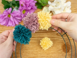 Someone attaching pompoms to a metal wreath form