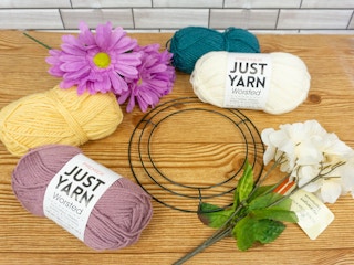 Materials for a spring wreath including fake flowers, different colored yarn, and a metal wreath form