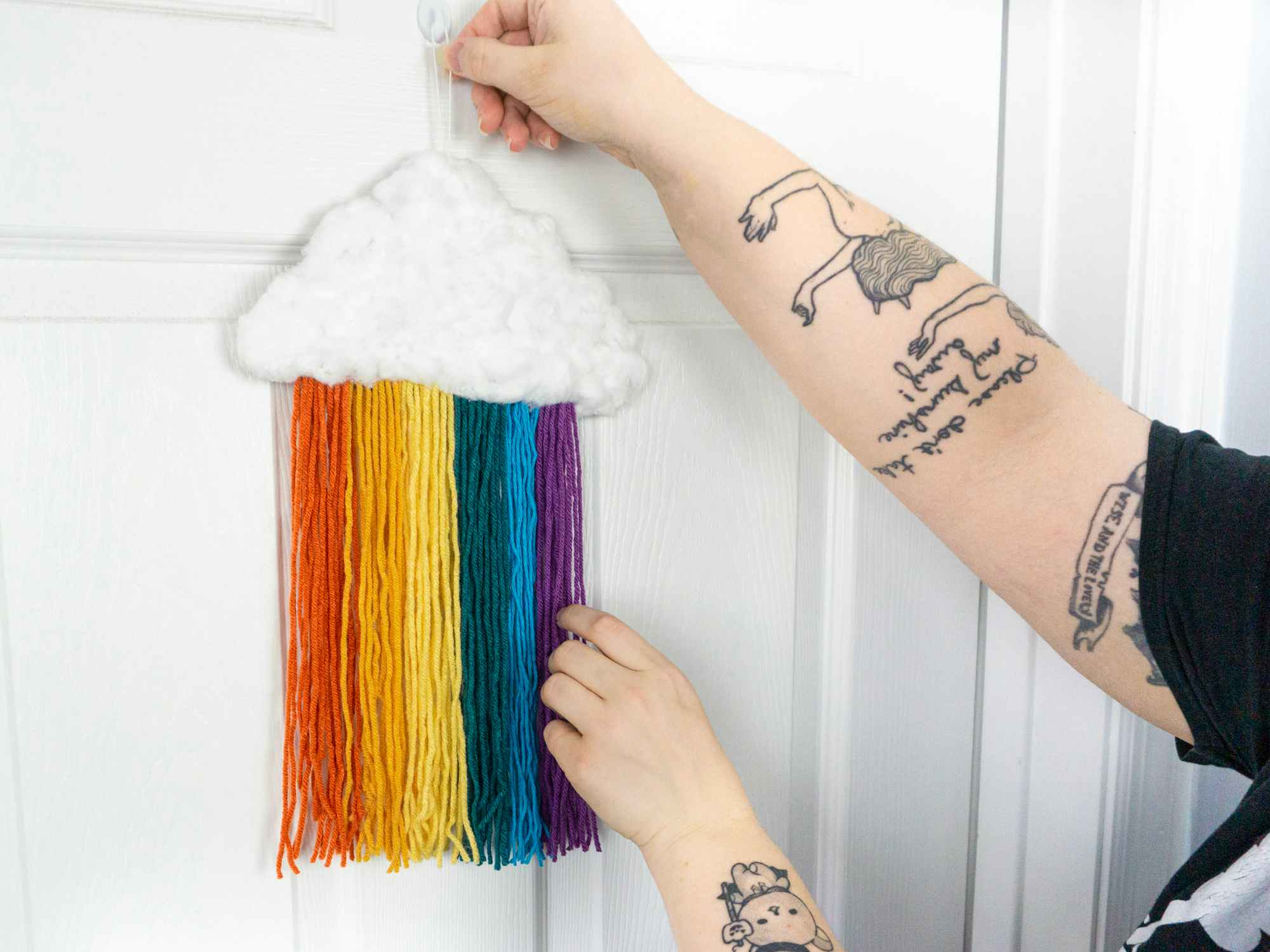 Someone hanging up a completed DIY rainbow cloud decoration