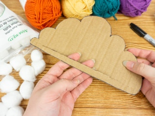 Someone sticking their fingers through a piece of cardboard to show the opening cut into the bottom of the cloud shape
