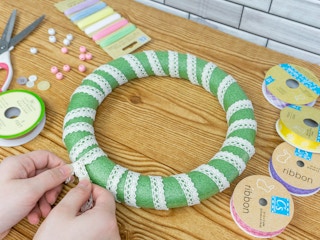 Someone tying ribbon onto a wreath form with more supplies on the table