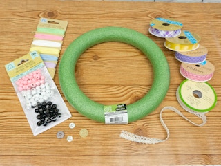 Materials for a spring wreath including several types of ribbon, wood beads, buttons, and a wreath form