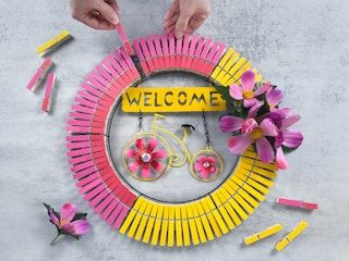 person making bright spring wreath with dollar tree garden sign and painted clothespins