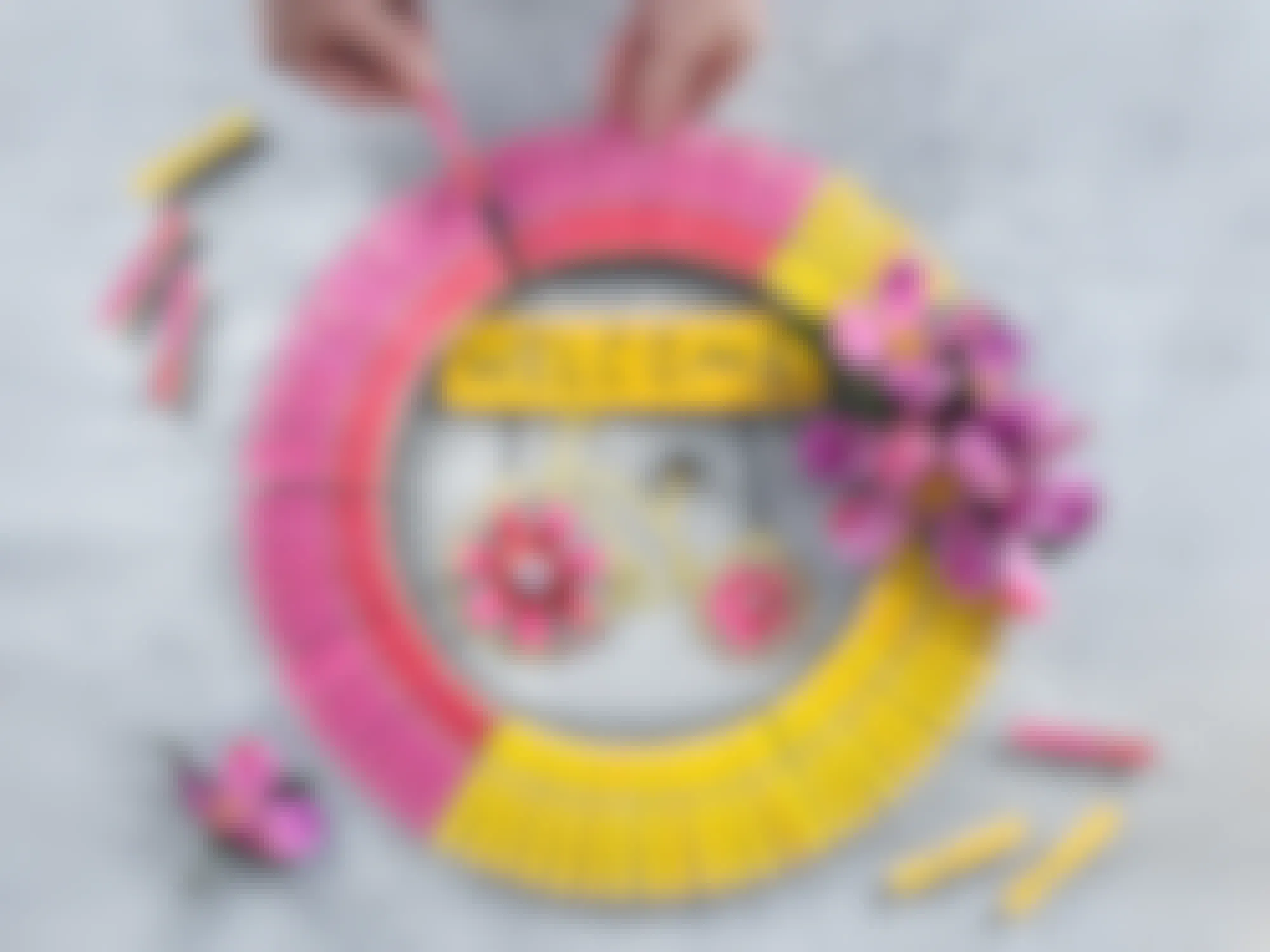 person making bright spring wreath with dollar tree garden sign and painted clothespins