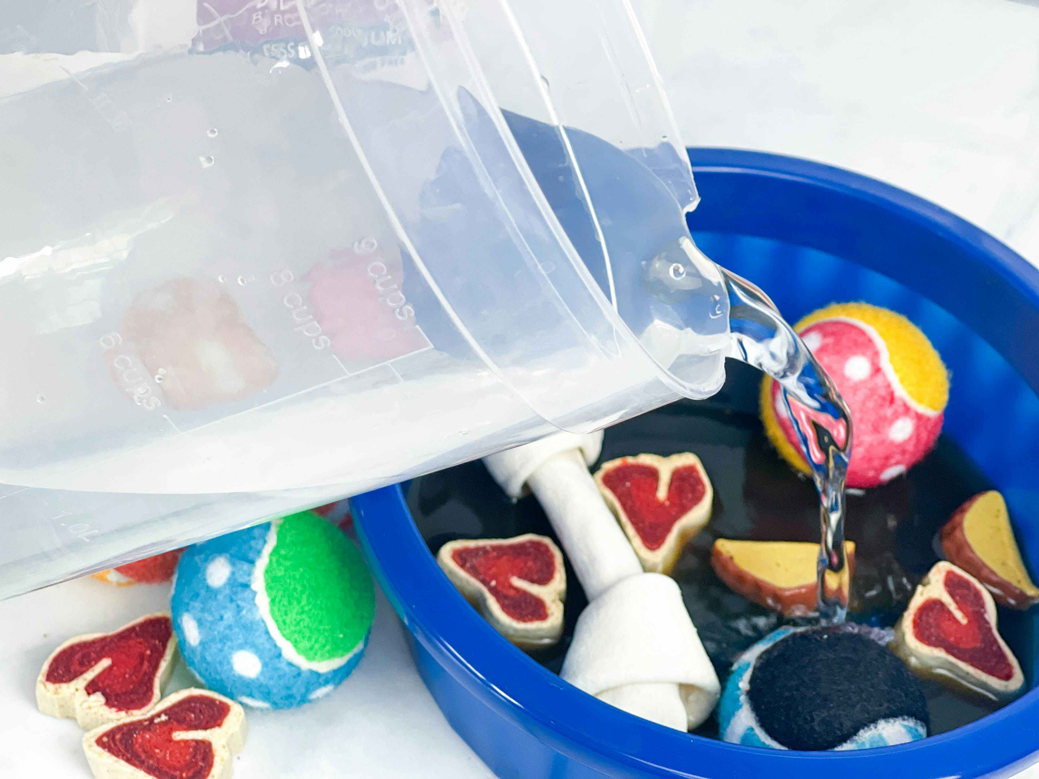 water being poured into a dog bowl filled with dog treats and toys 