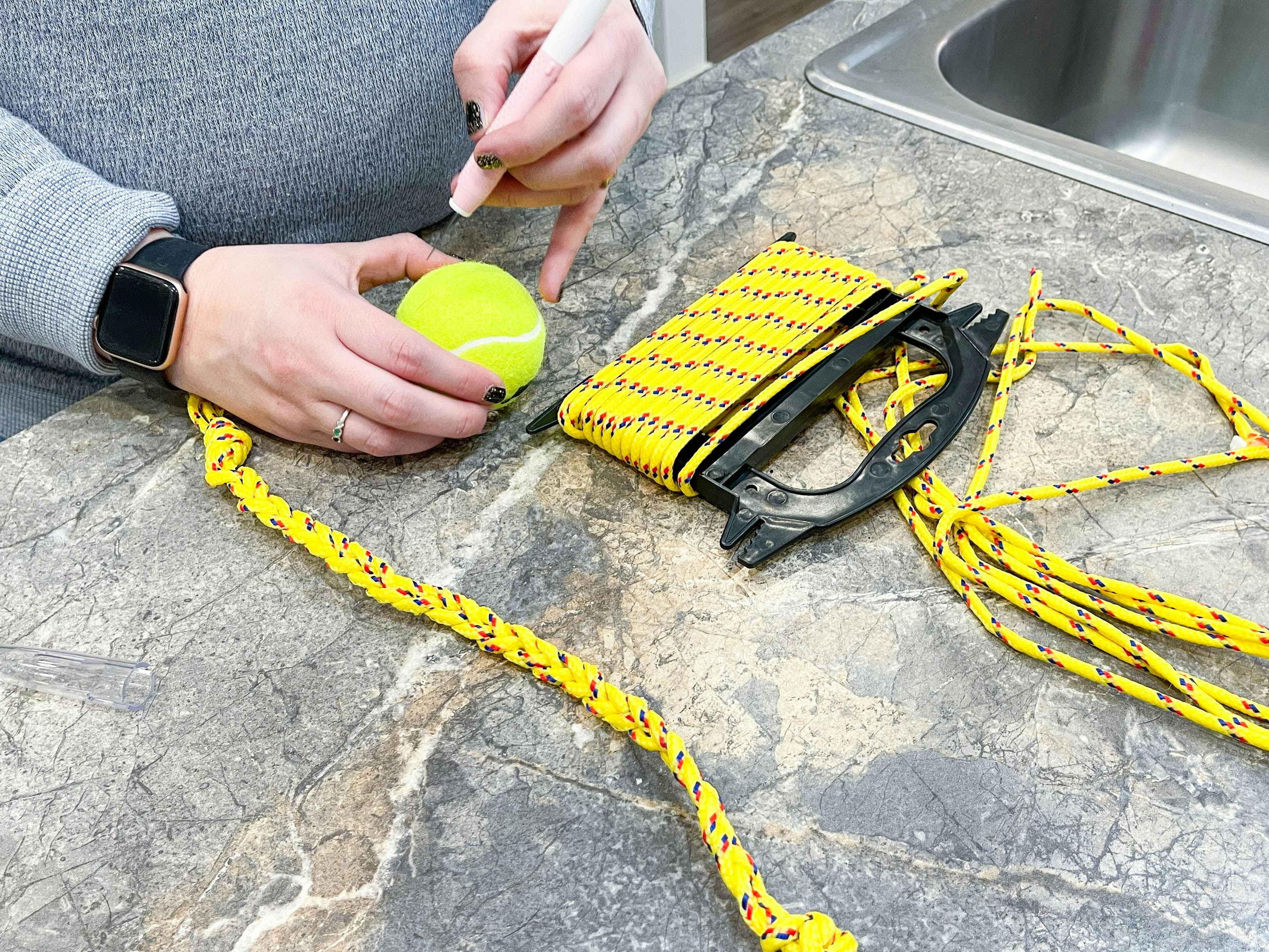 a person cutting a tennis ball next to rope to make a diy dog toy 